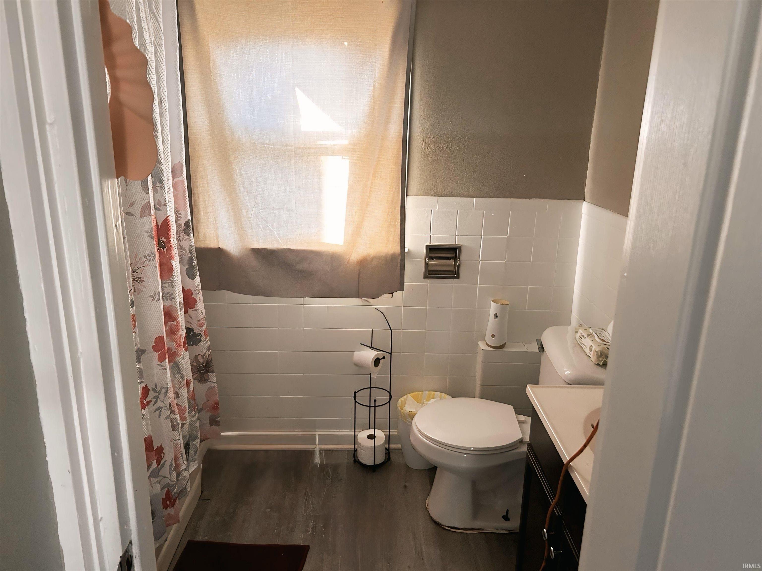 Full bath with vanity, a shower with shower curtain, dark wood-style floors, tile walls, and a wainscoted wall