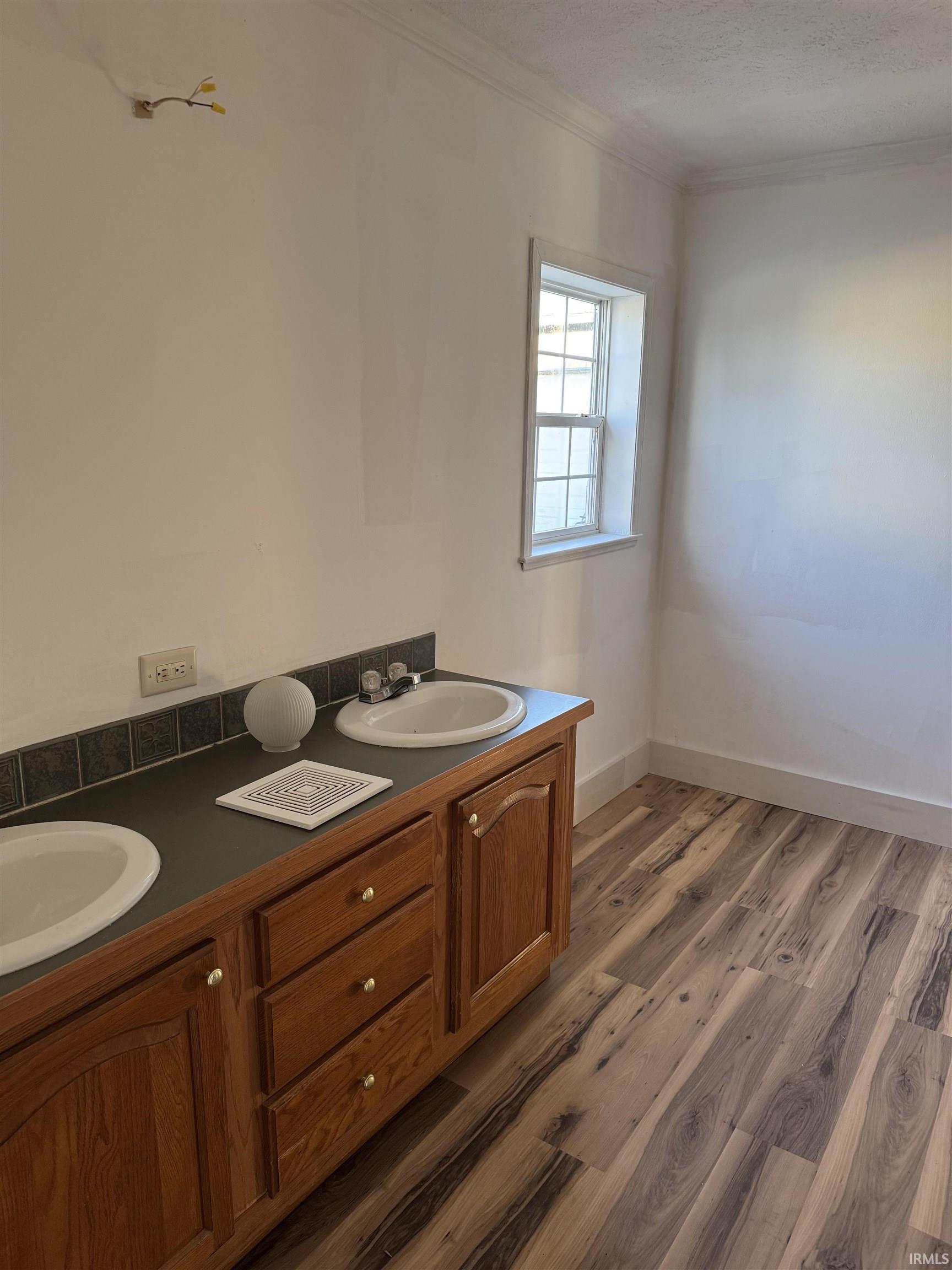 Full bathroom featuring double vanity, light wood finished floors, a textured ceiling, and crown molding