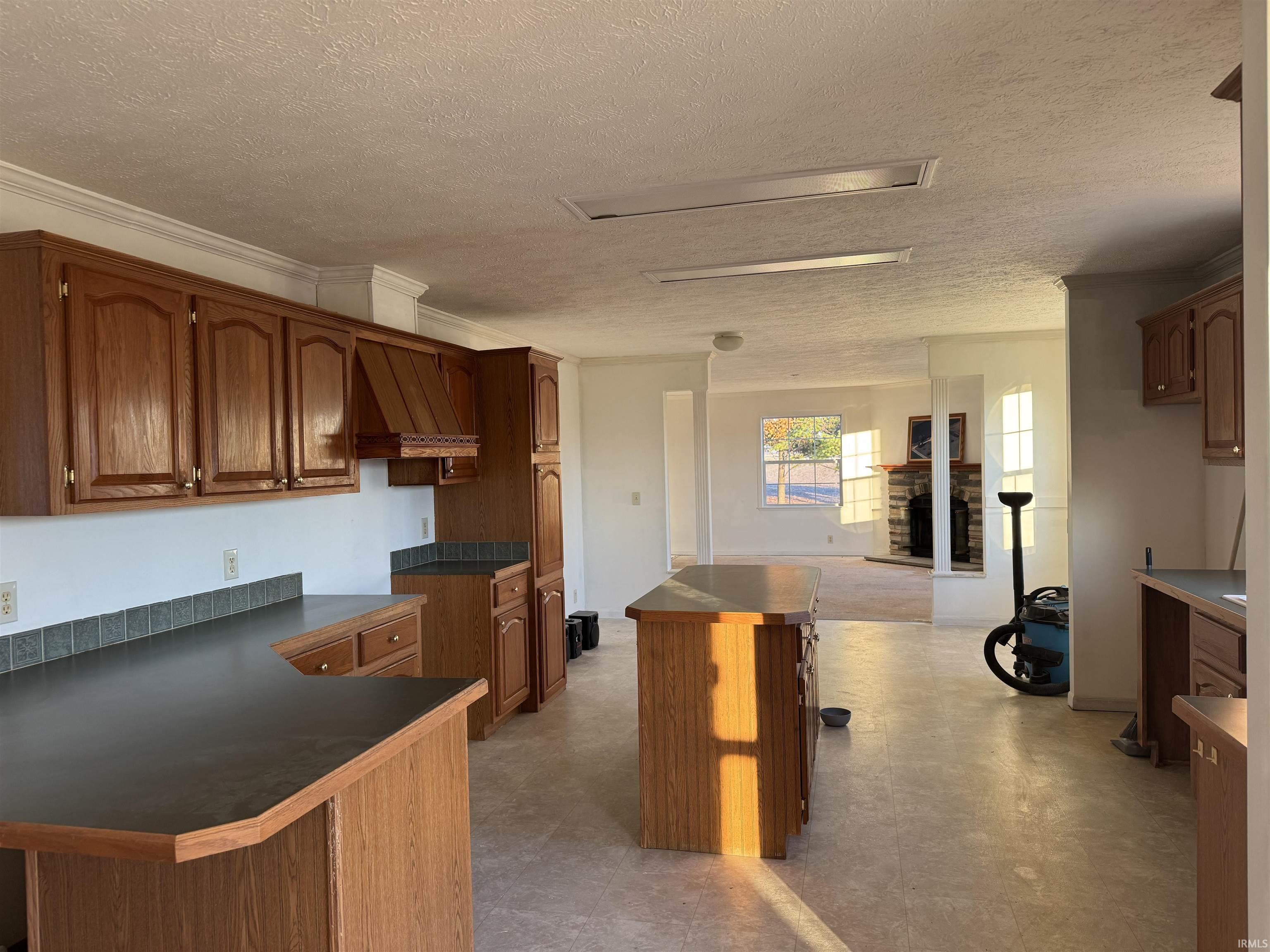 Kitchen featuring brown cabinets, dark countertops, light floors, a textured ceiling, and crown molding