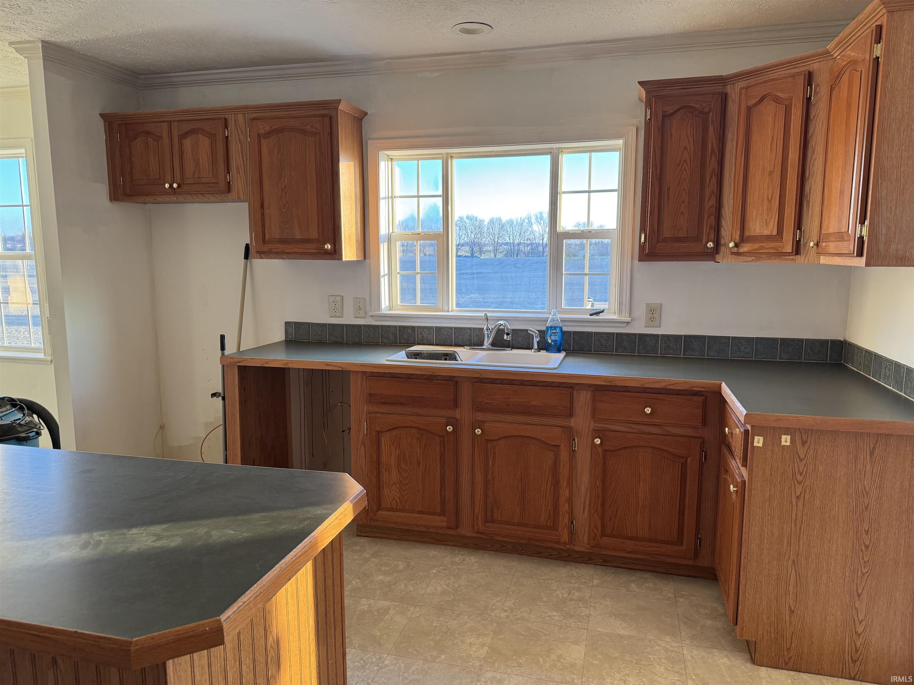 Kitchen with dark countertops, brown cabinetry, crown molding, and a textured ceiling