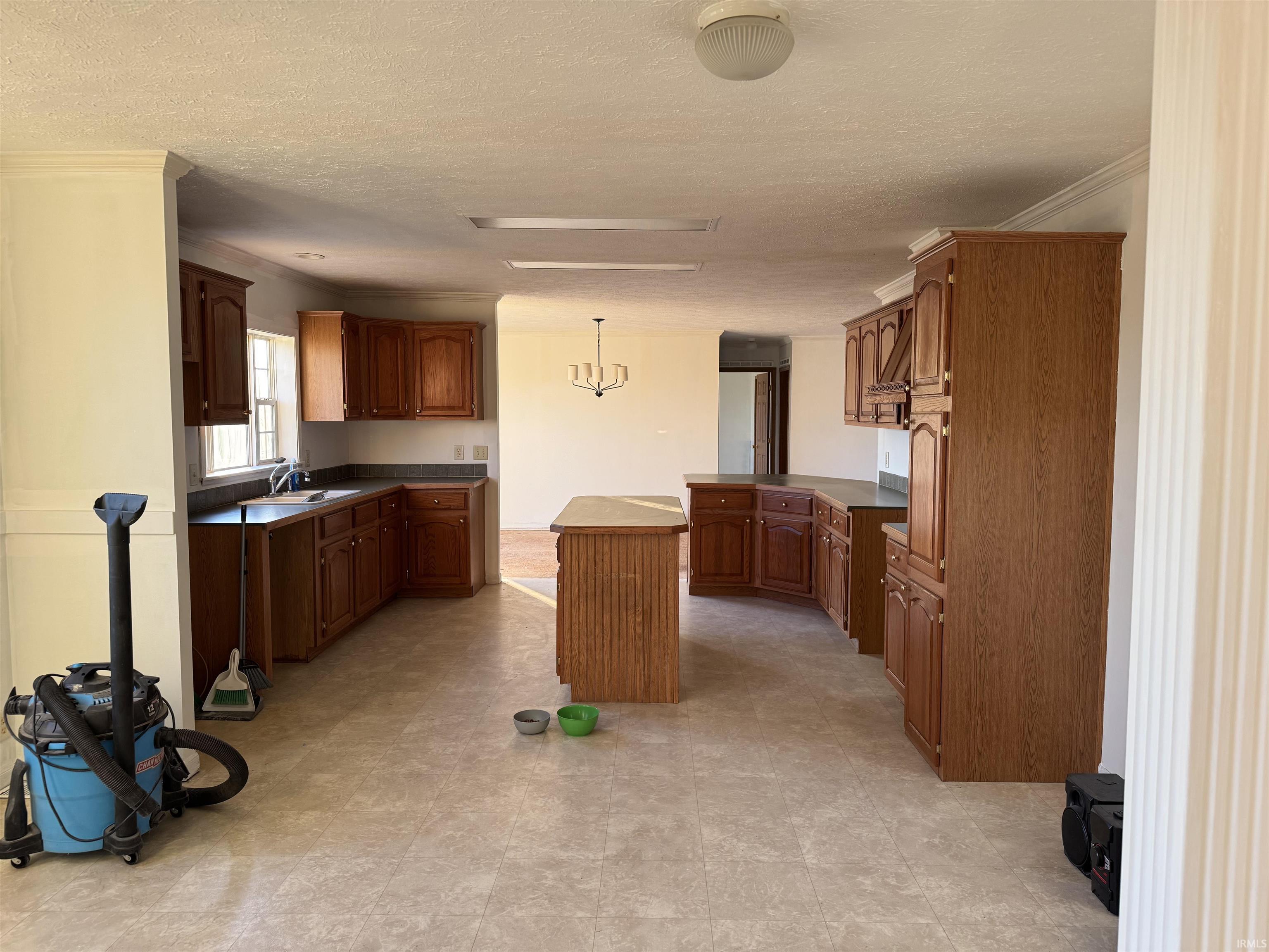 Kitchen with pendant lighting, brown cabinetry, a textured ceiling, dark countertops, and a kitchen island