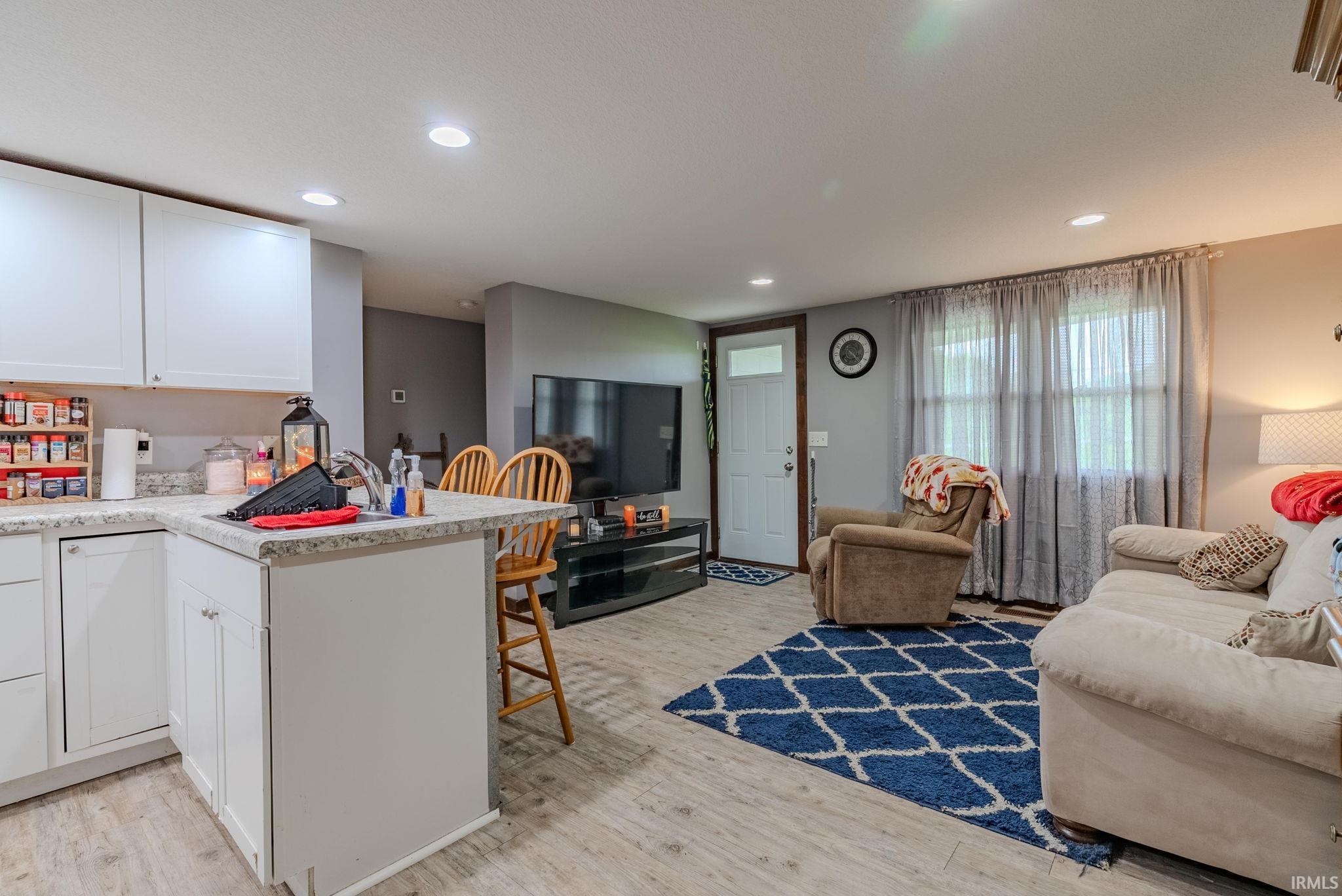 Kitchen with a breakfast bar area, white cabinetry, open floor plan, light wood-type laminate flooring, and a peninsula
