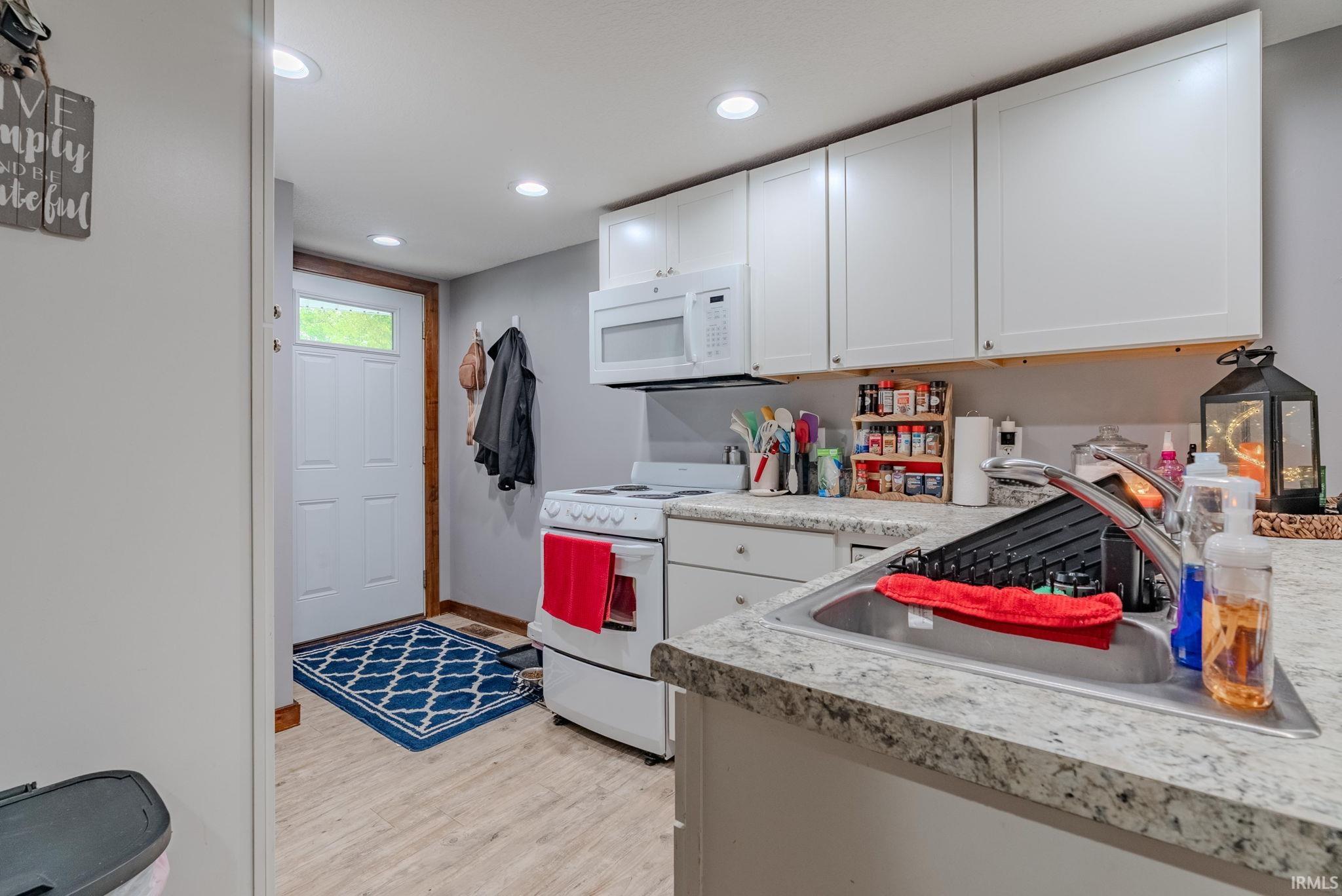 Kitchen with white appliances, light countertops, white cabinets, light wood-style laminate floors, and recessed lighting