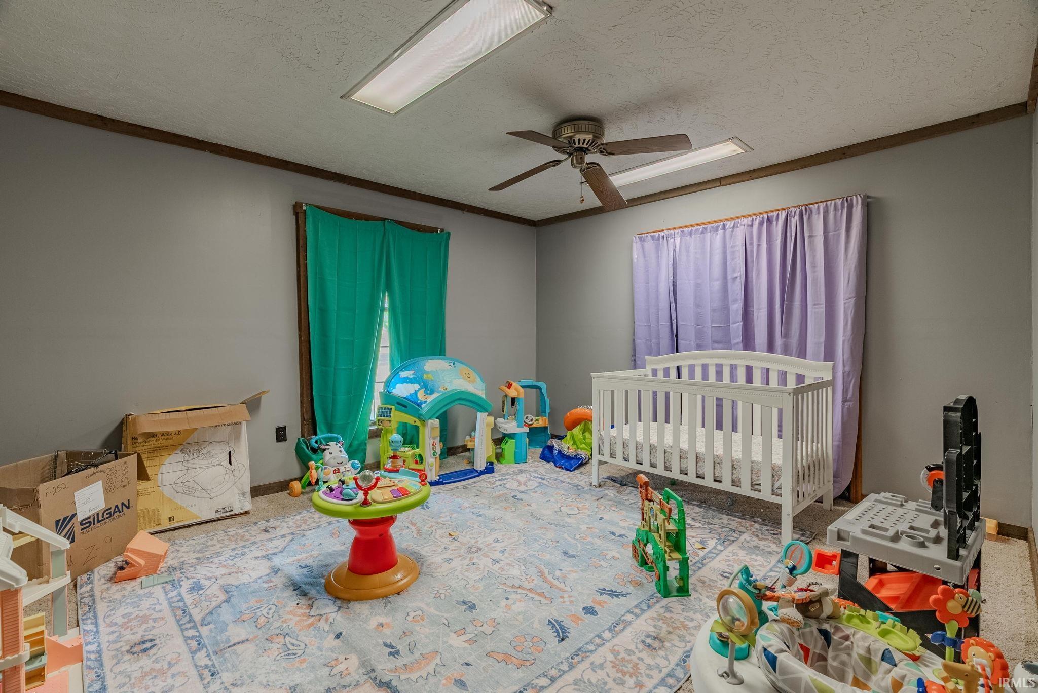Bedroom with a crib, a textured ceiling, a ceiling fan, and ornamental molding