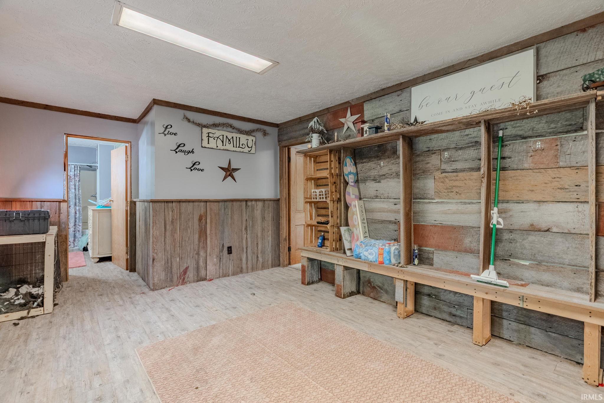 Mudroom featuring wood walls, laminate floors, wainscoting, ornamental molding, and a textured ceiling