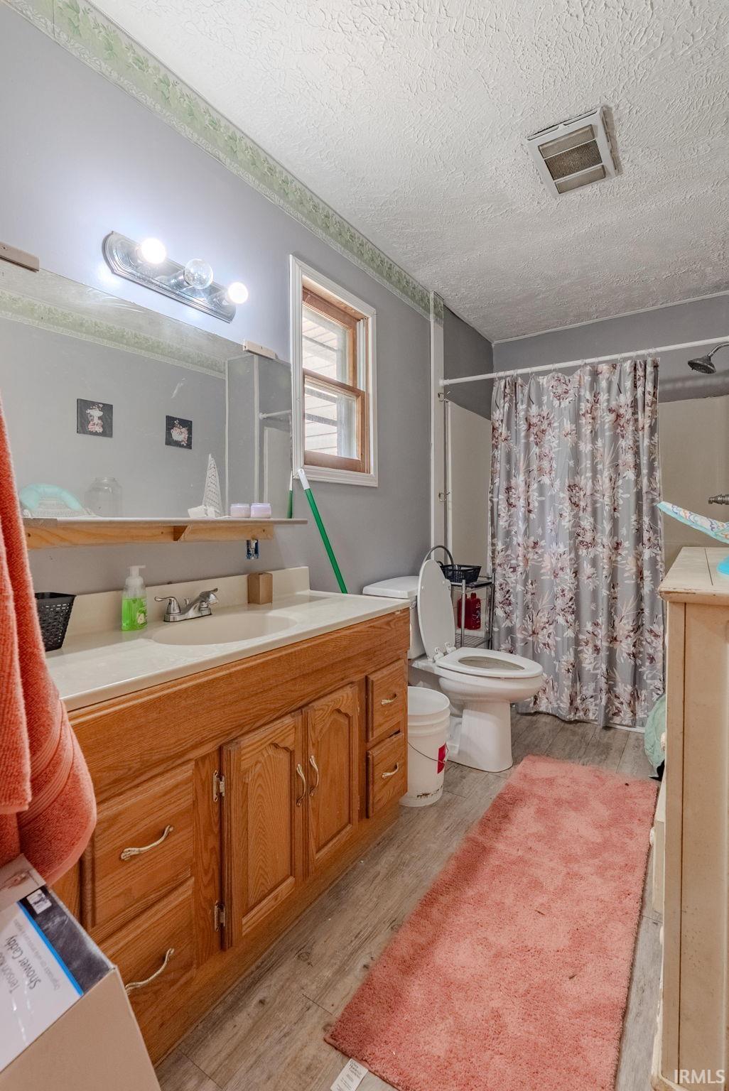 Full bath with vanity, light wood-style laminate flooring, and a textured ceiling
