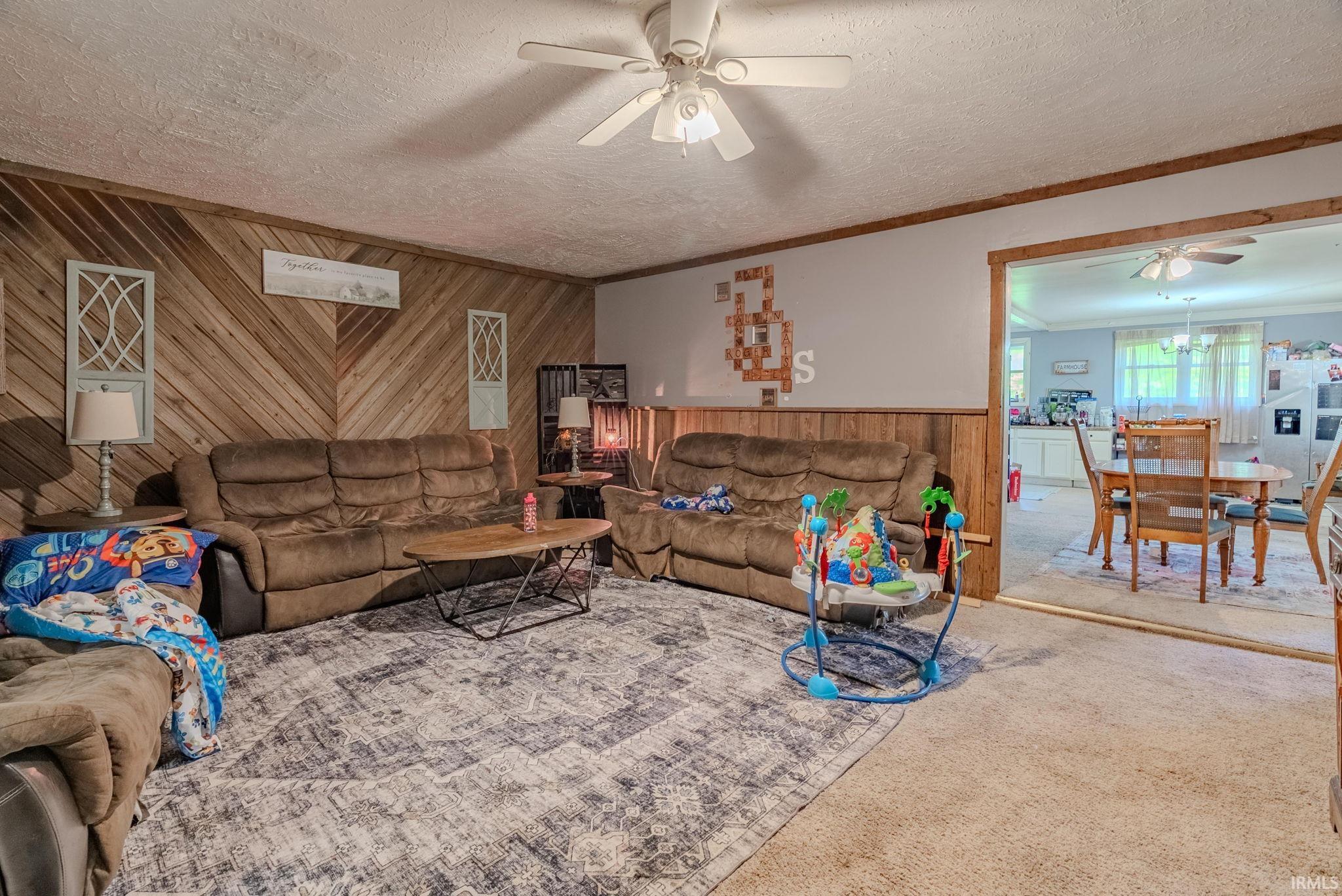 Living room featuring wood walls, ceiling fan, carpet flooring, a textured ceiling, and crown molding