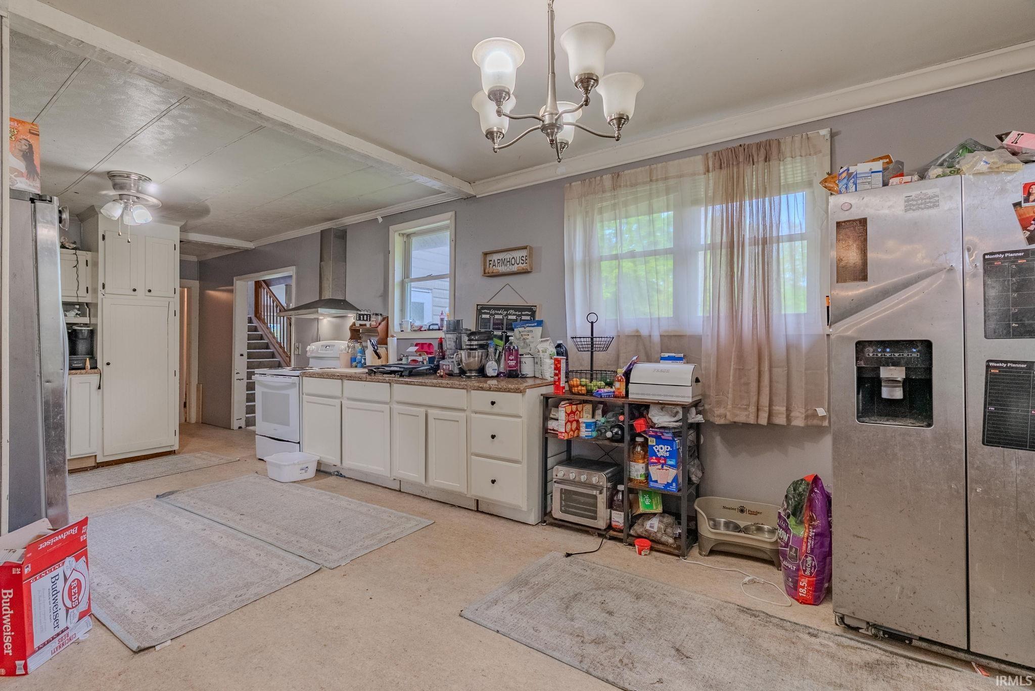 Kitchen with stainless steel fridge, electric stove, white cabinetry, decorative light fixtures, and wall exhaust hood