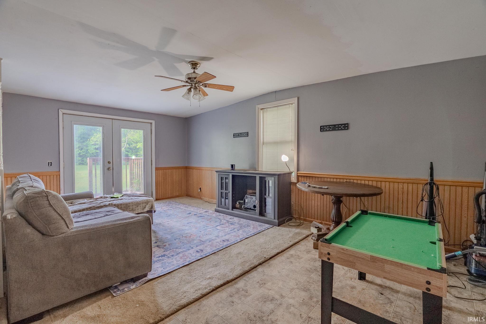 Living area featuring wainscoting, wood walls, ceiling fan, and french doors