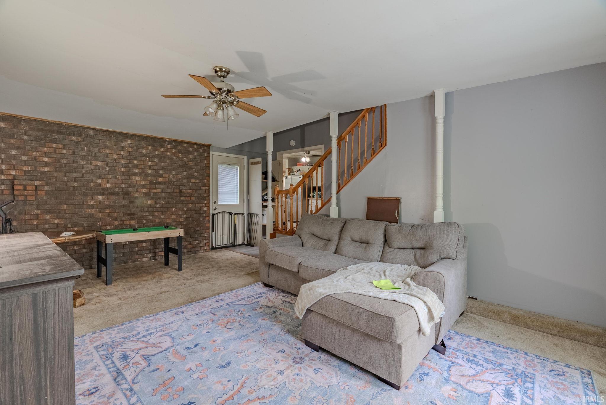 Living area featuring ceiling fan, brick wall, and stairs