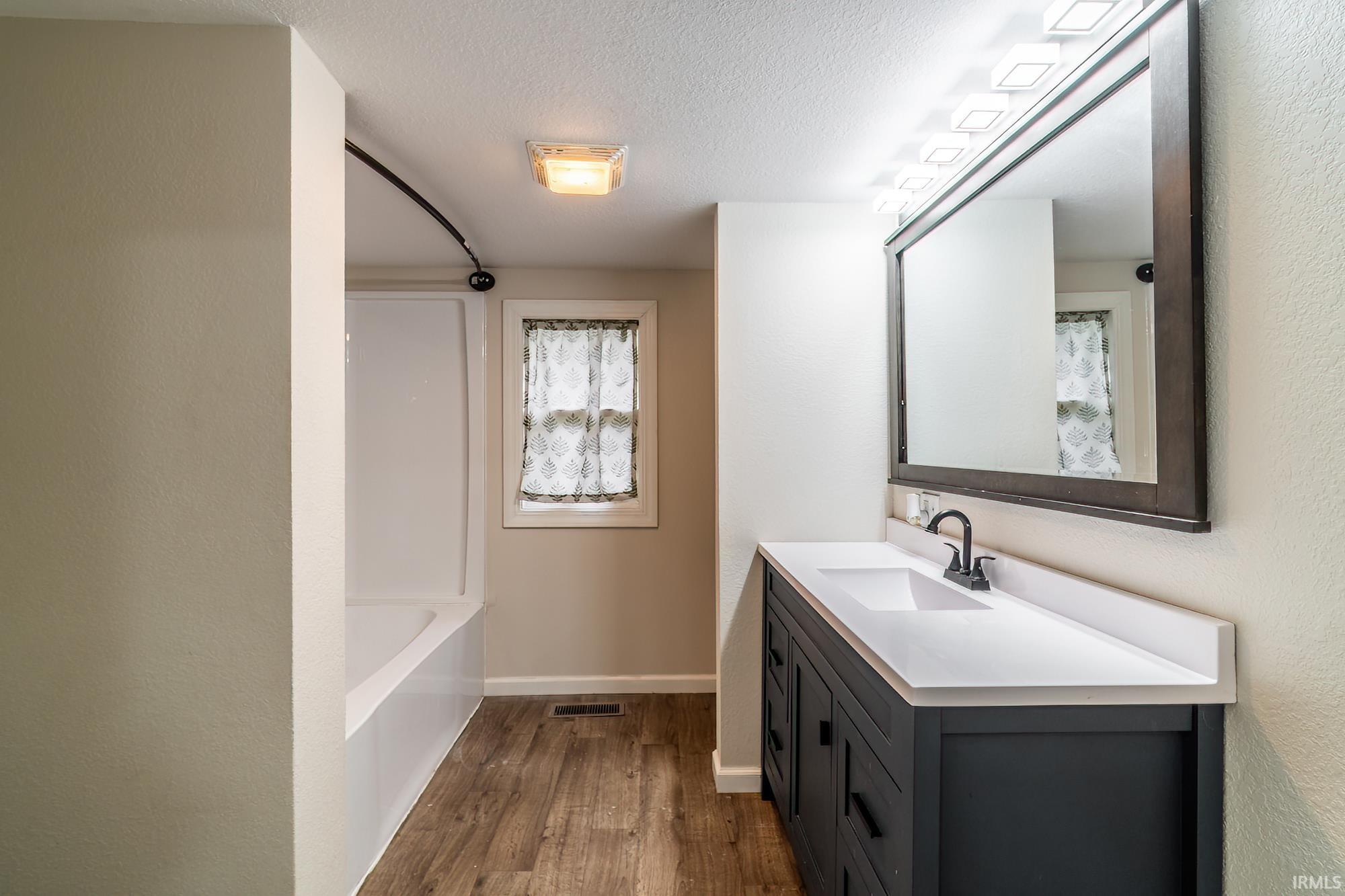 Full bath featuring vanity, a textured ceiling, dark wood-type flooring, shower / bath combination with curtain, and a textured wall