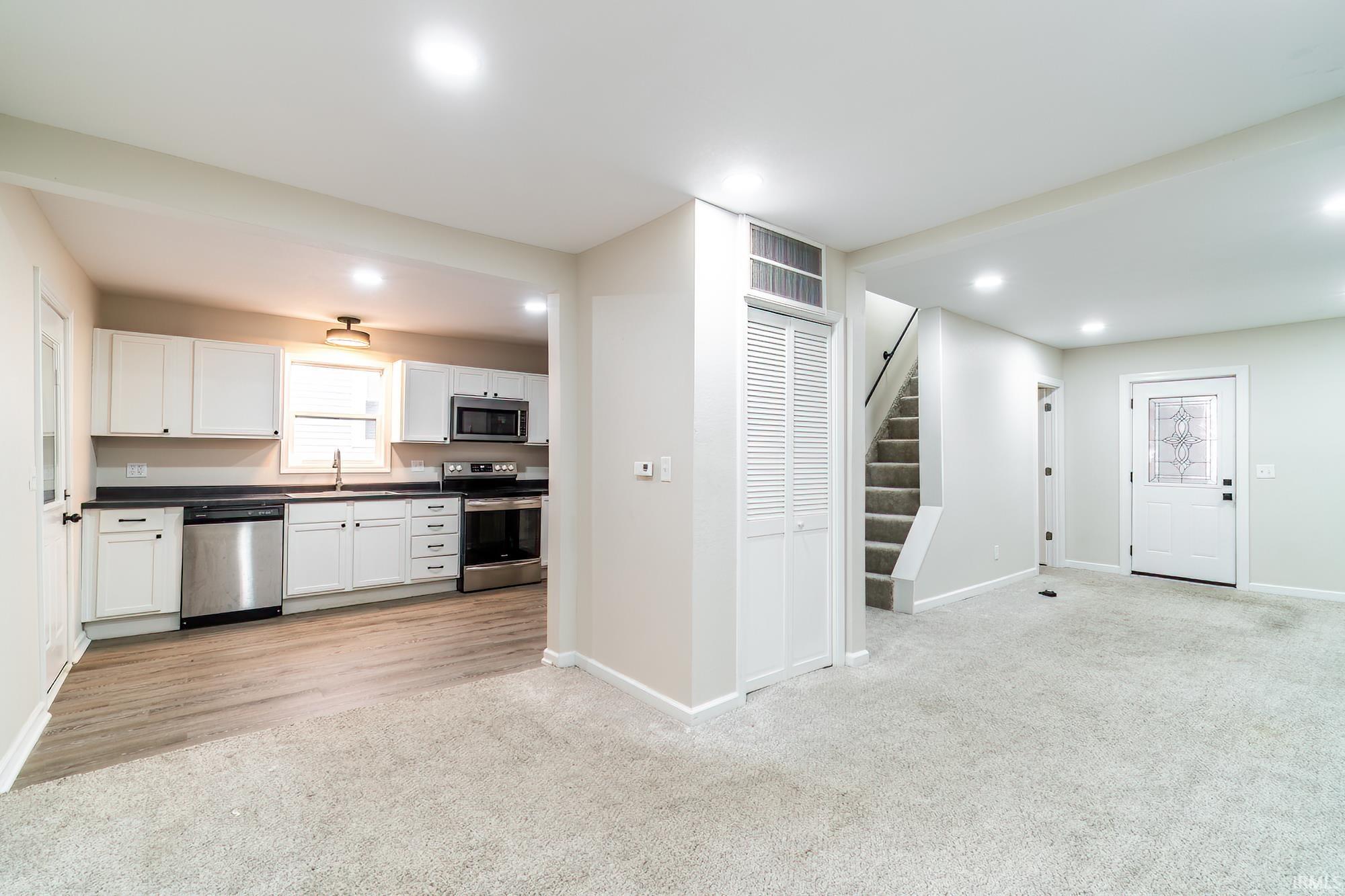 Kitchen with light carpet, white cabinets, appliances with stainless steel finishes, dark countertops, and recessed lighting