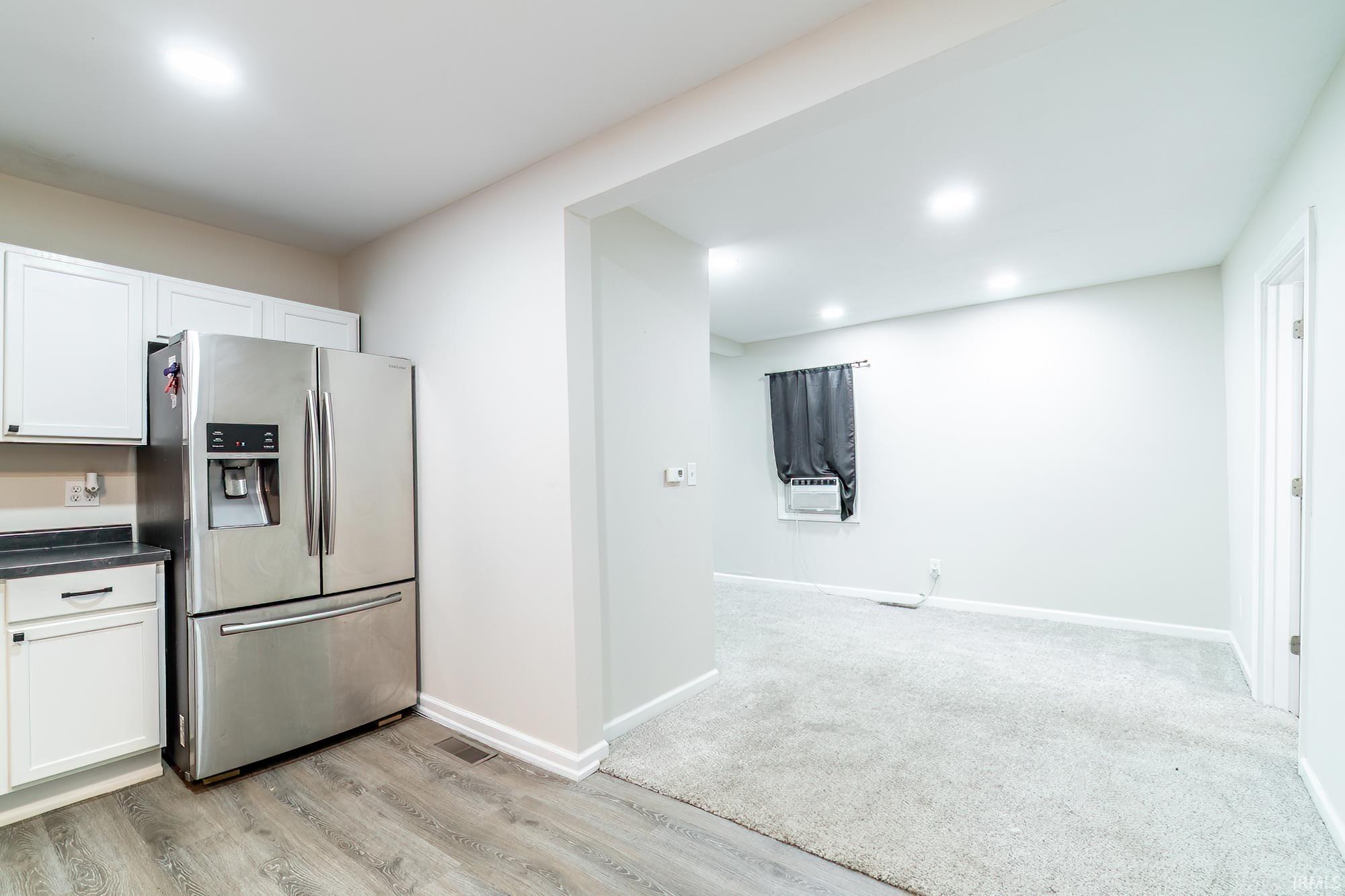 Kitchen with stainless steel fridge, dark countertops, white cabinetry, recessed lighting, and cooling unit