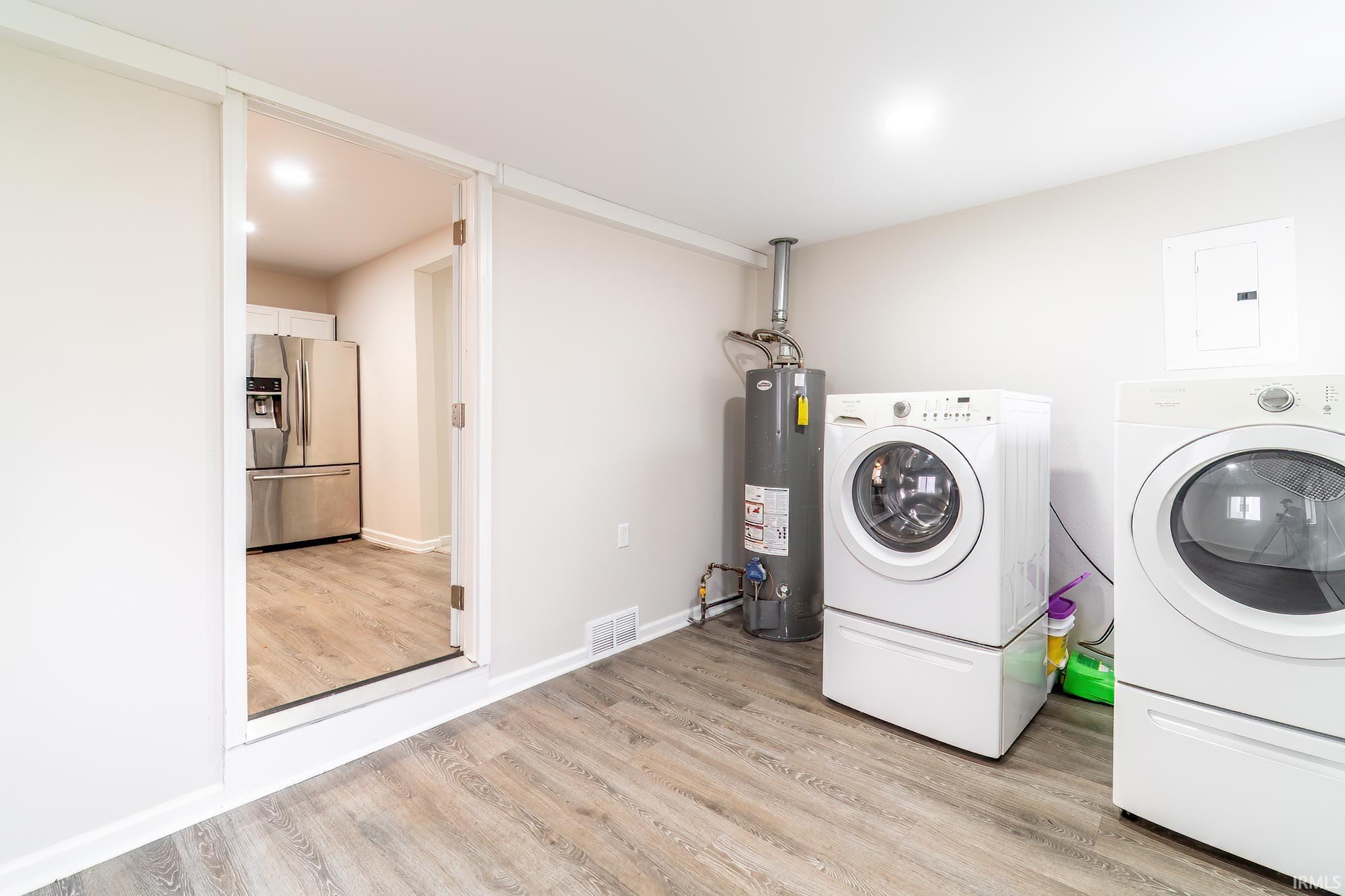 Laundry area with washer and dryer, water heater, light wood-style flooring, and electric panel