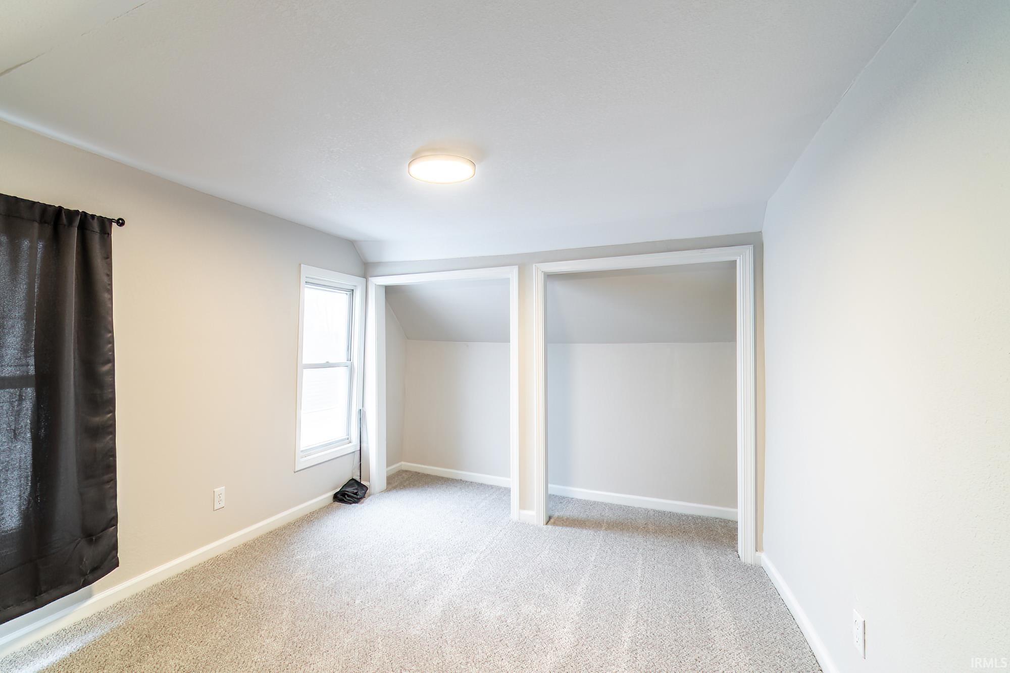 Unfurnished bedroom featuring two closets, vaulted ceiling, and light colored carpet