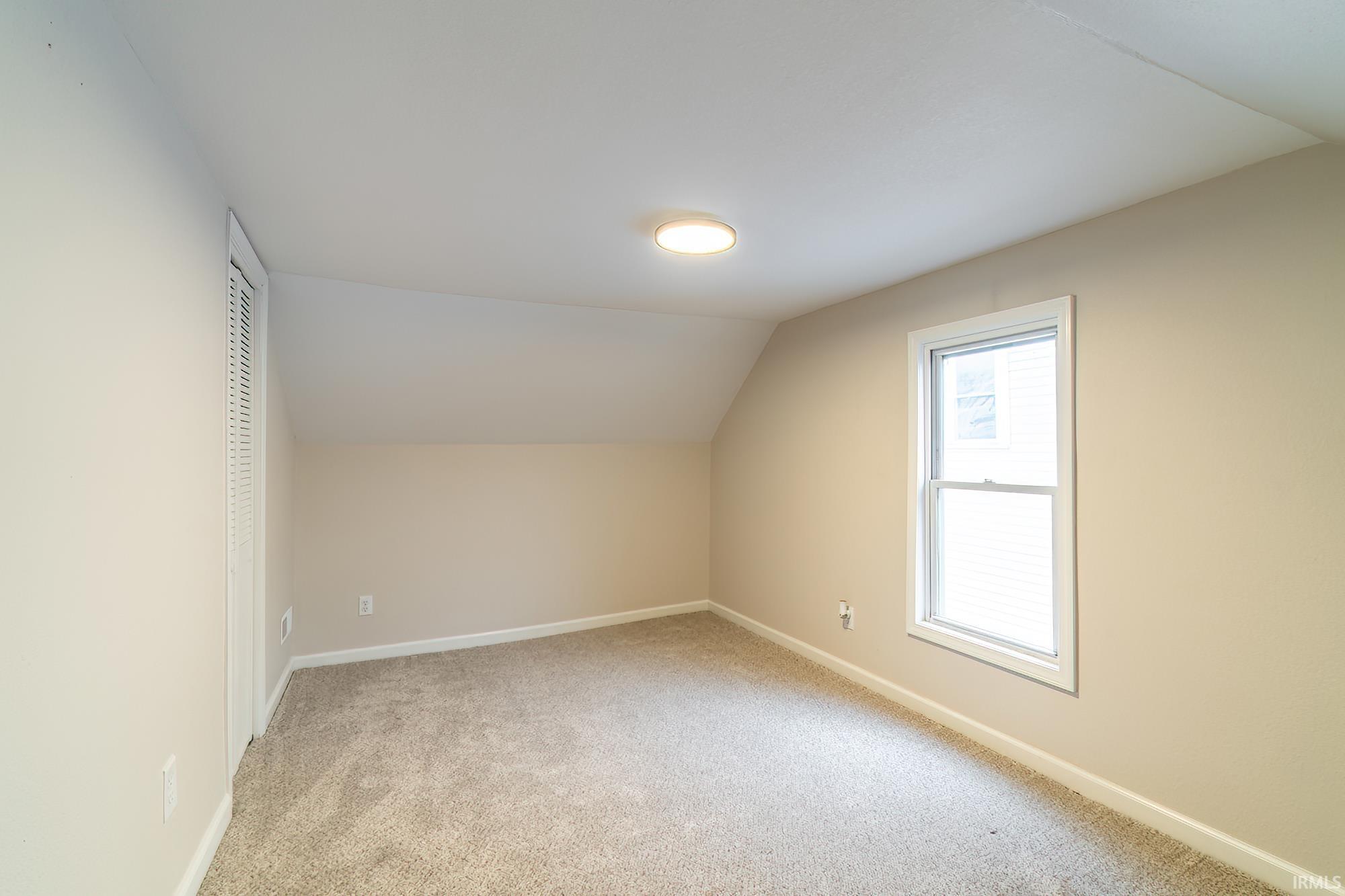 Additional living space featuring vaulted ceiling and light carpet