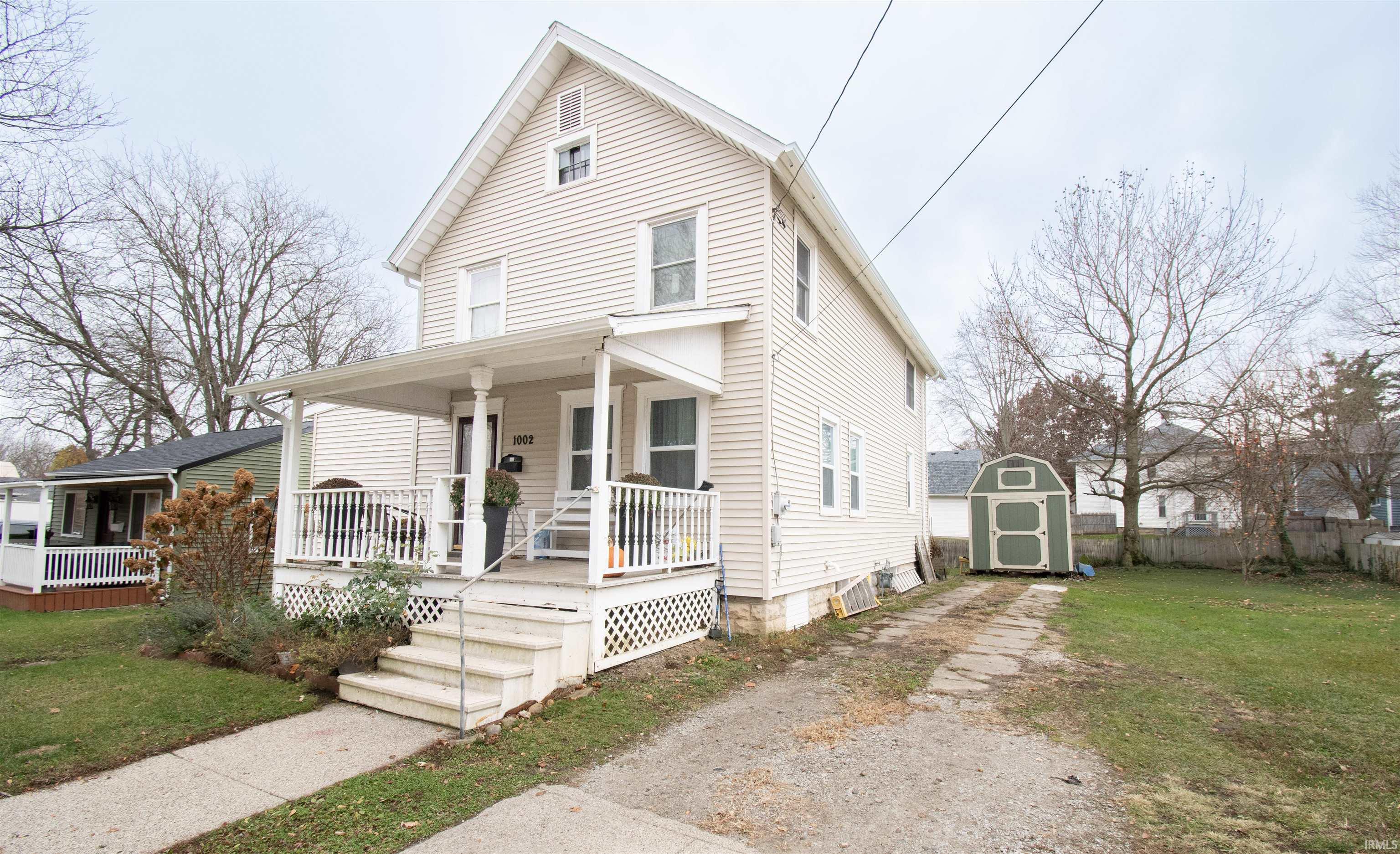 View of front facade with covered porch, a shed, and driveway