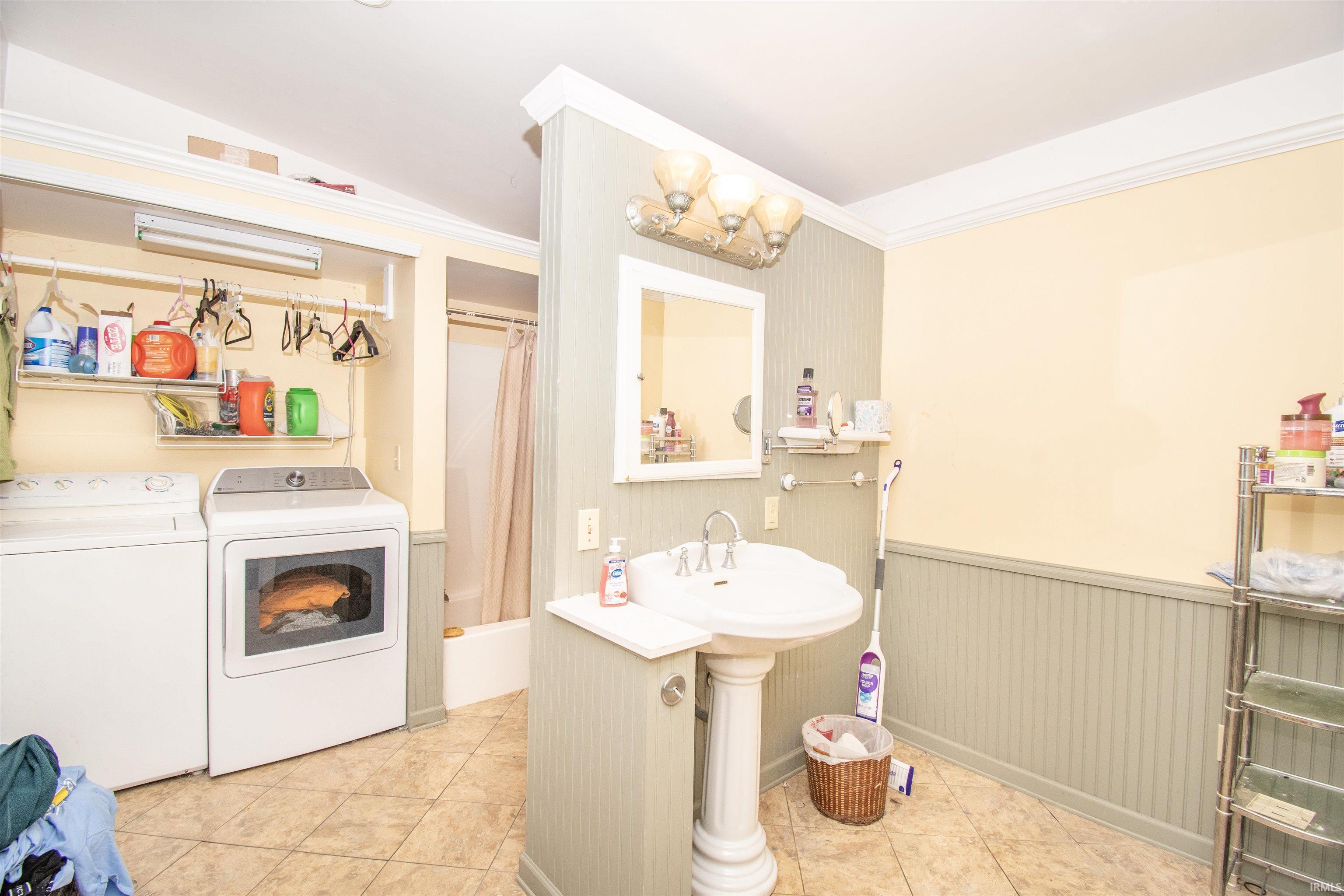 Bathroom with a wainscoted wall, shower / bath combo, ornamental molding, light tile patterned flooring, and washing machine and dryer