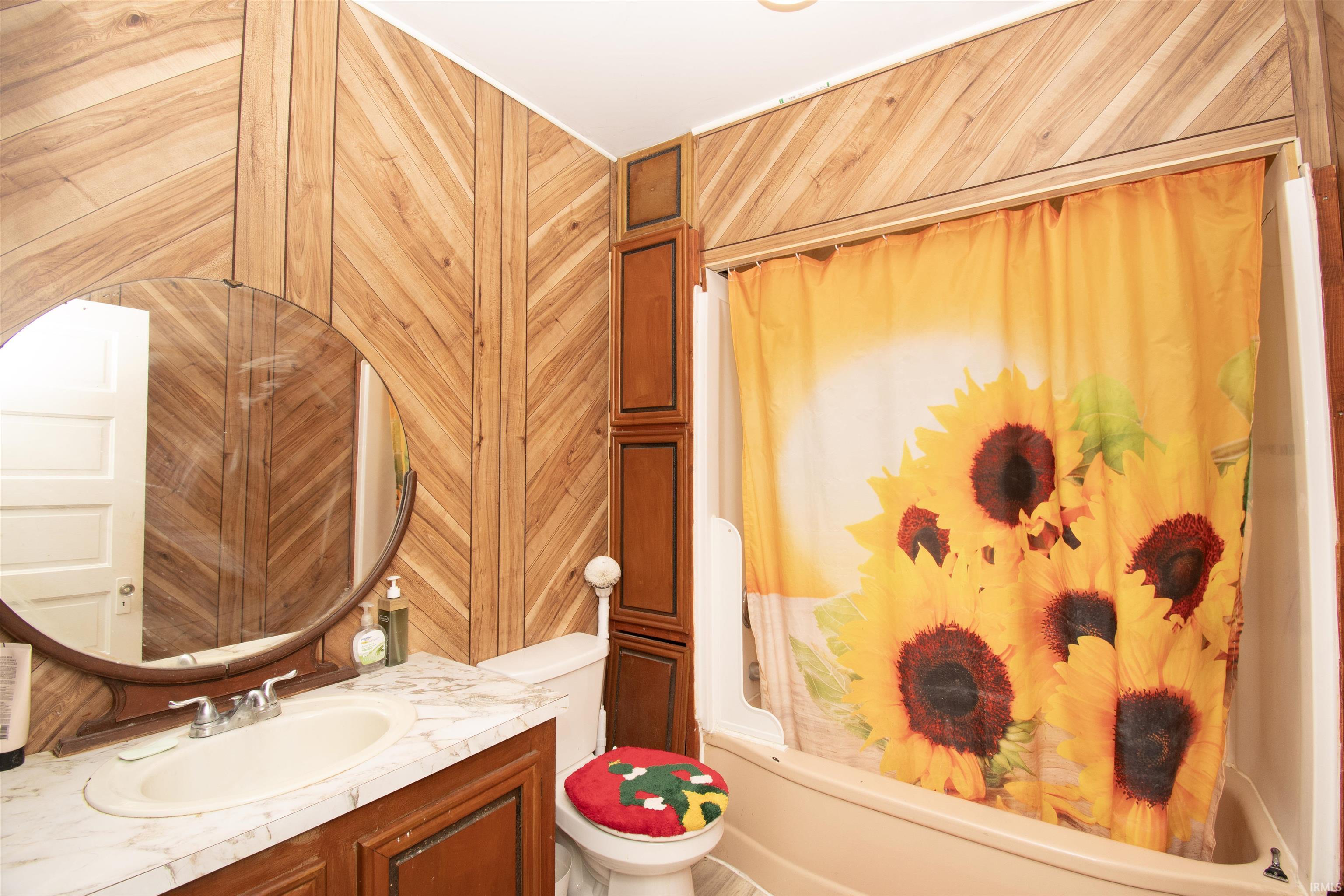 Full bath featuring vanity, wooden walls, and shower / bath combo with shower curtain