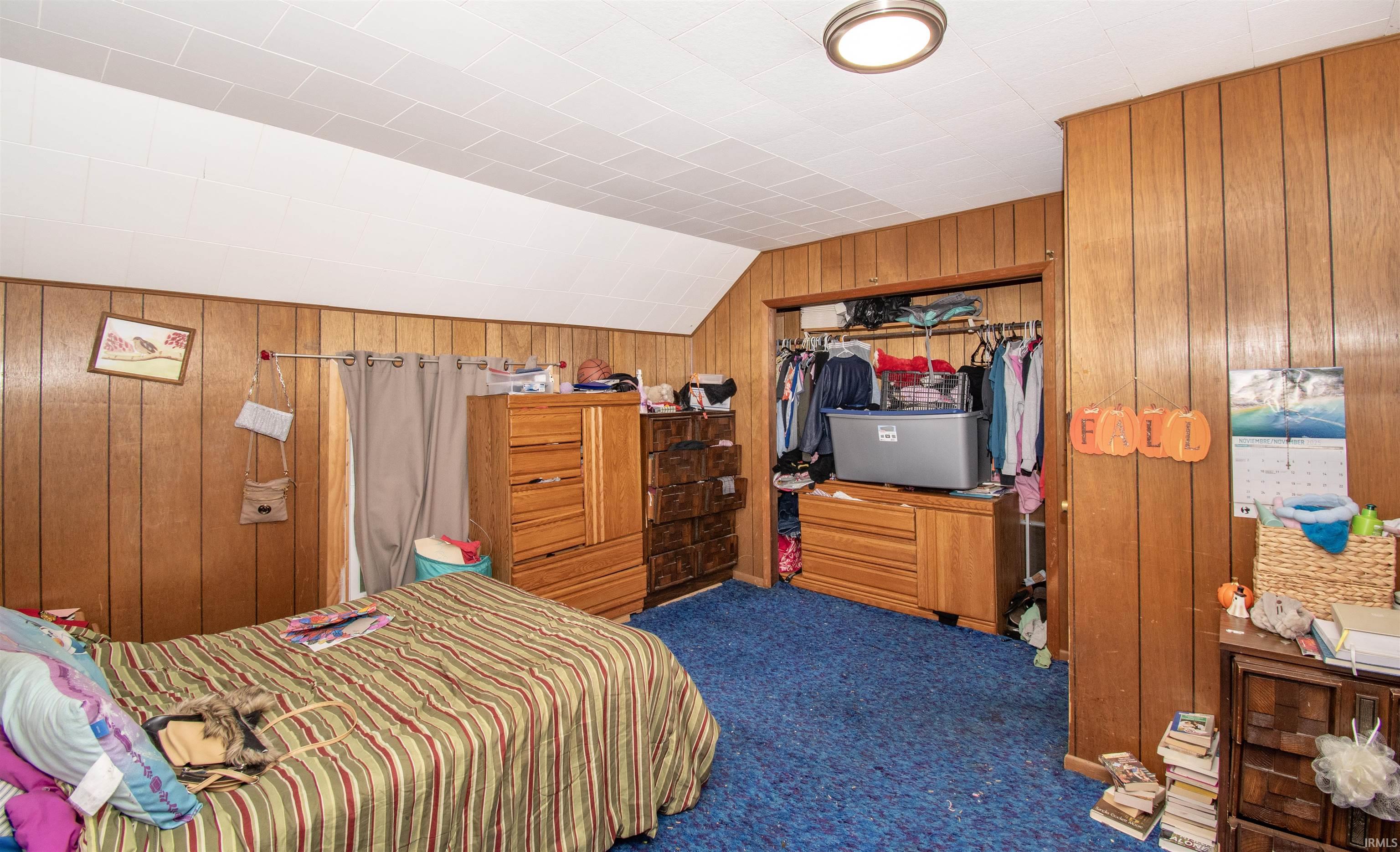 Carpeted bedroom featuring wood walls, lofted ceiling, and a closet