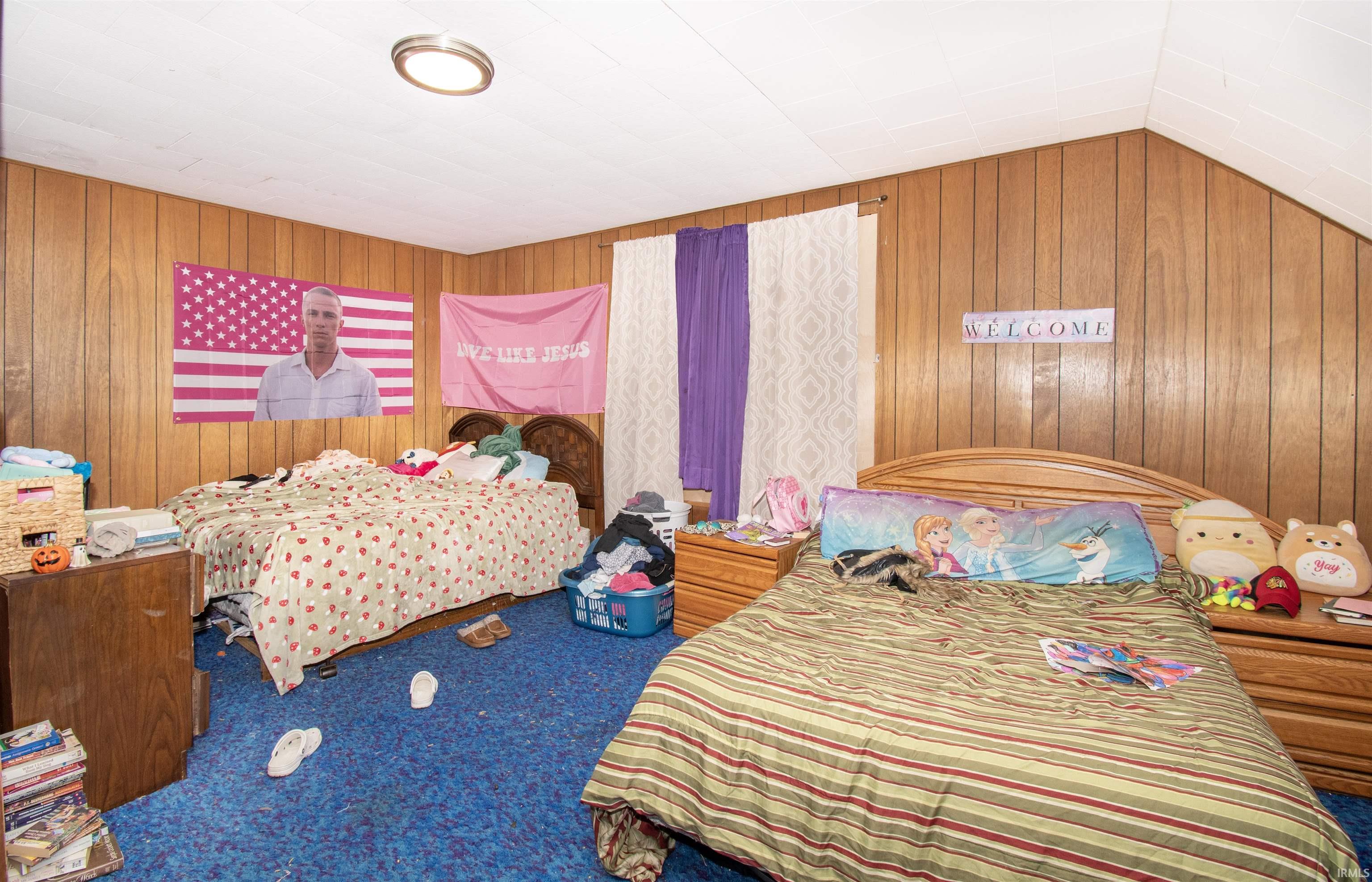 Bedroom with carpet floors, wooden walls, and lofted ceiling