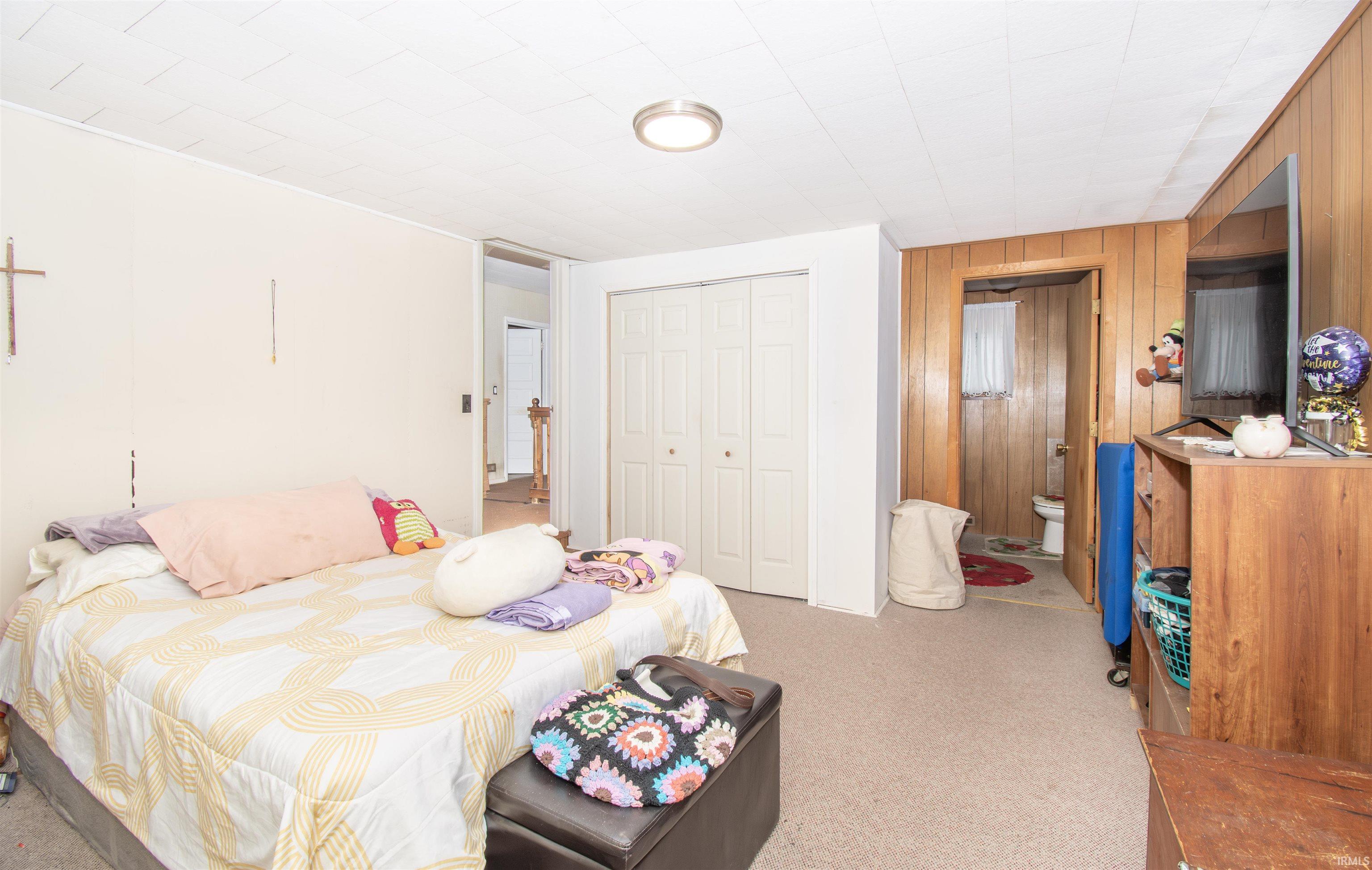 Bedroom featuring a closet, ensuite bathroom, light carpet, and wood walls