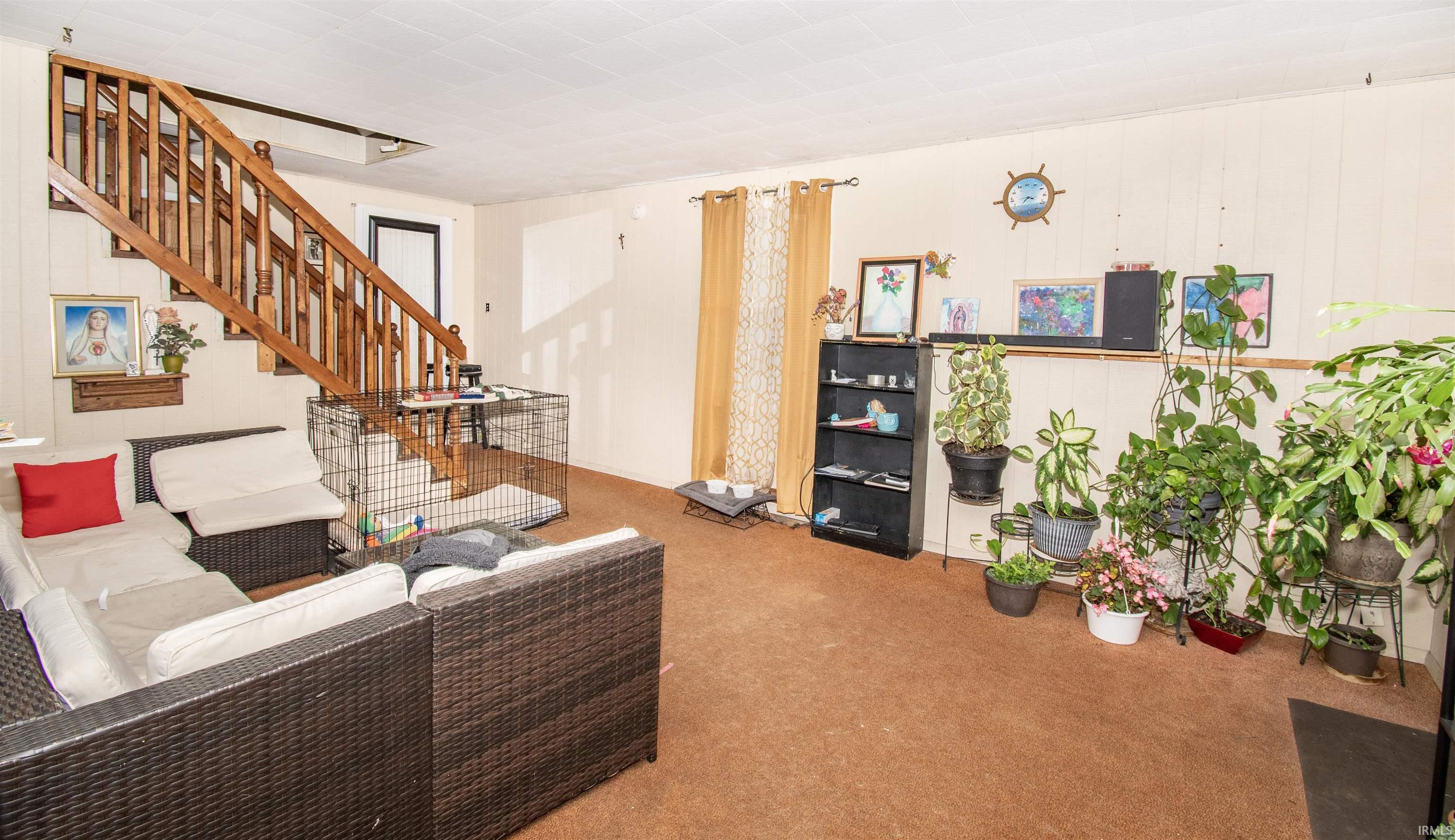 Carpeted living area featuring wooden walls and stairs