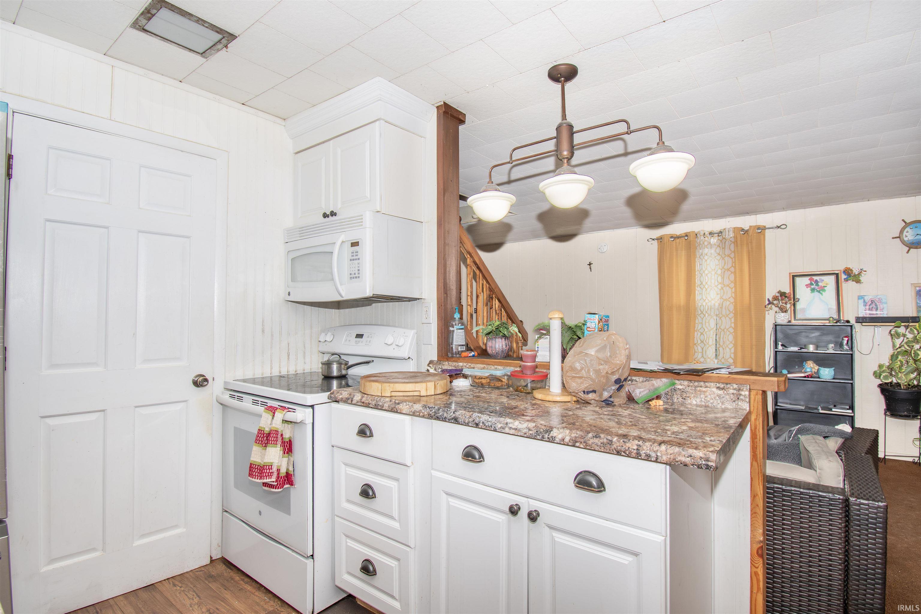 Kitchen with white appliances, white cabinets, decorative light fixtures, dark wood finished floors, and dark stone counters