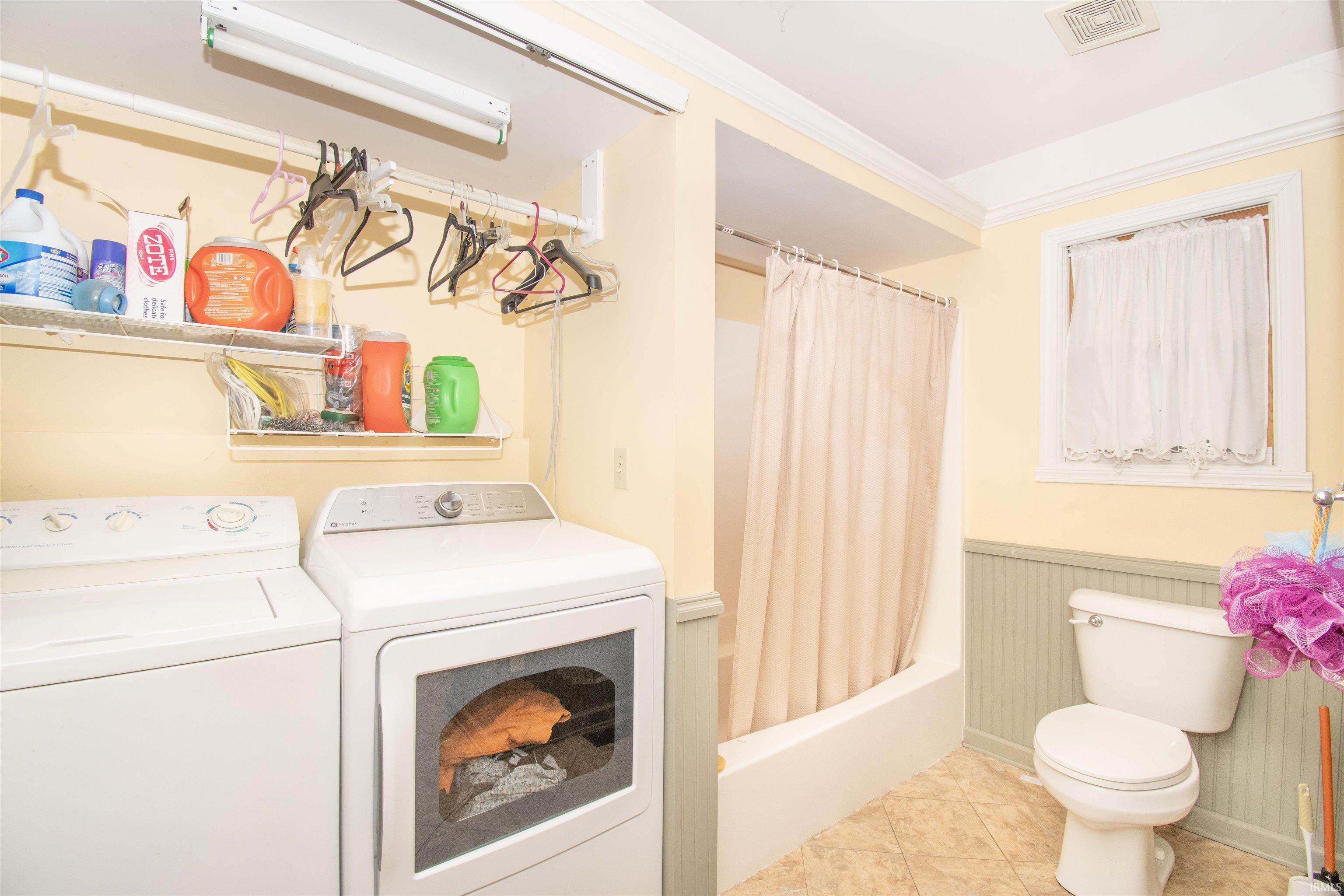 Laundry room featuring wainscoting, crown molding, washer and clothes dryer, and light tile patterned floors