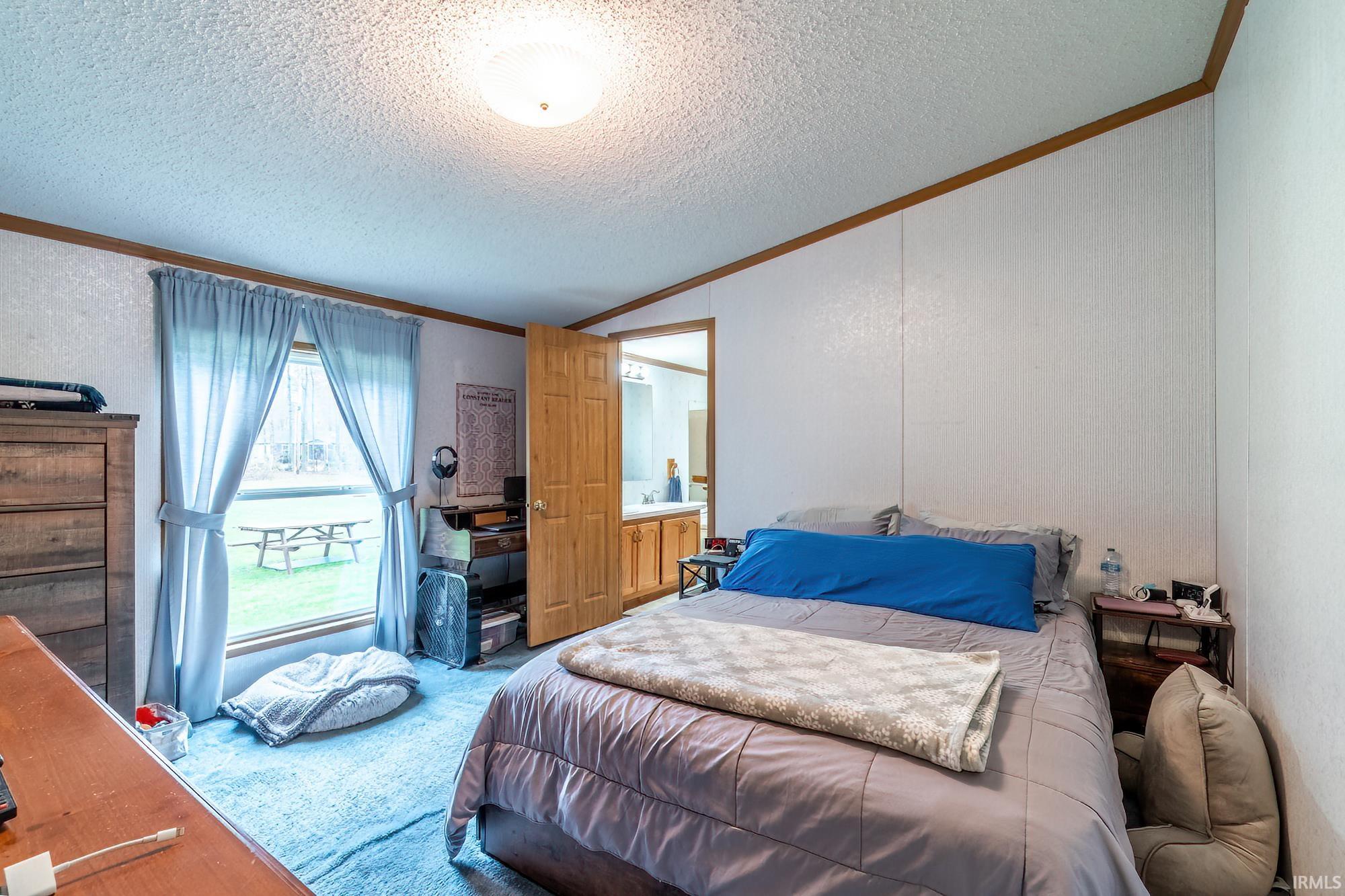 Bedroom with crown molding, lofted ceiling, a textured ceiling, a textured wall, and carpet