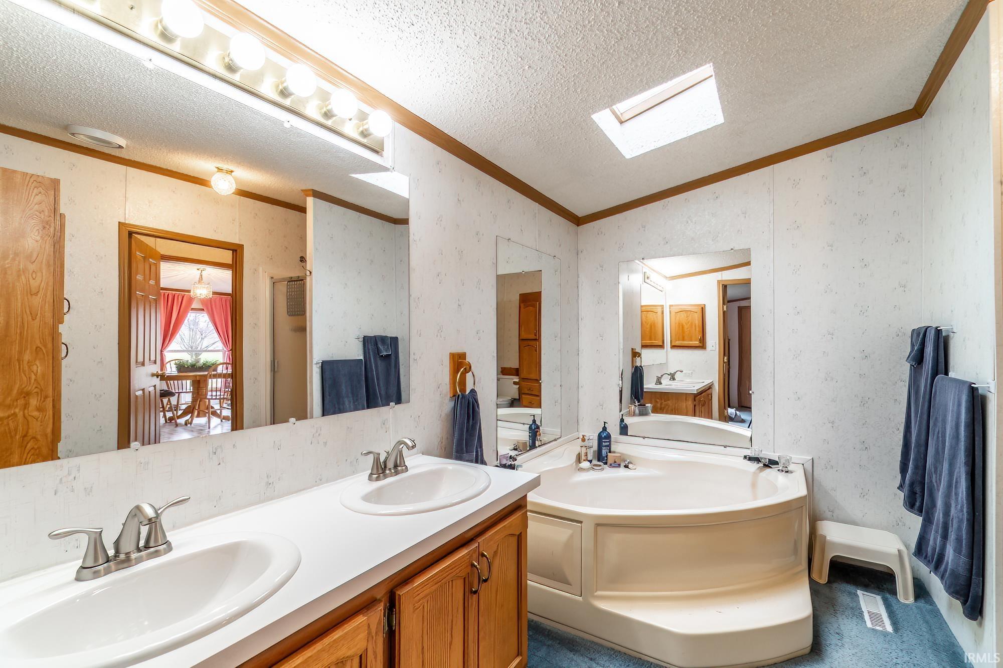 Bathroom featuring double vanity, a garden tub, a textured ceiling, wallpapered walls, and lofted ceiling