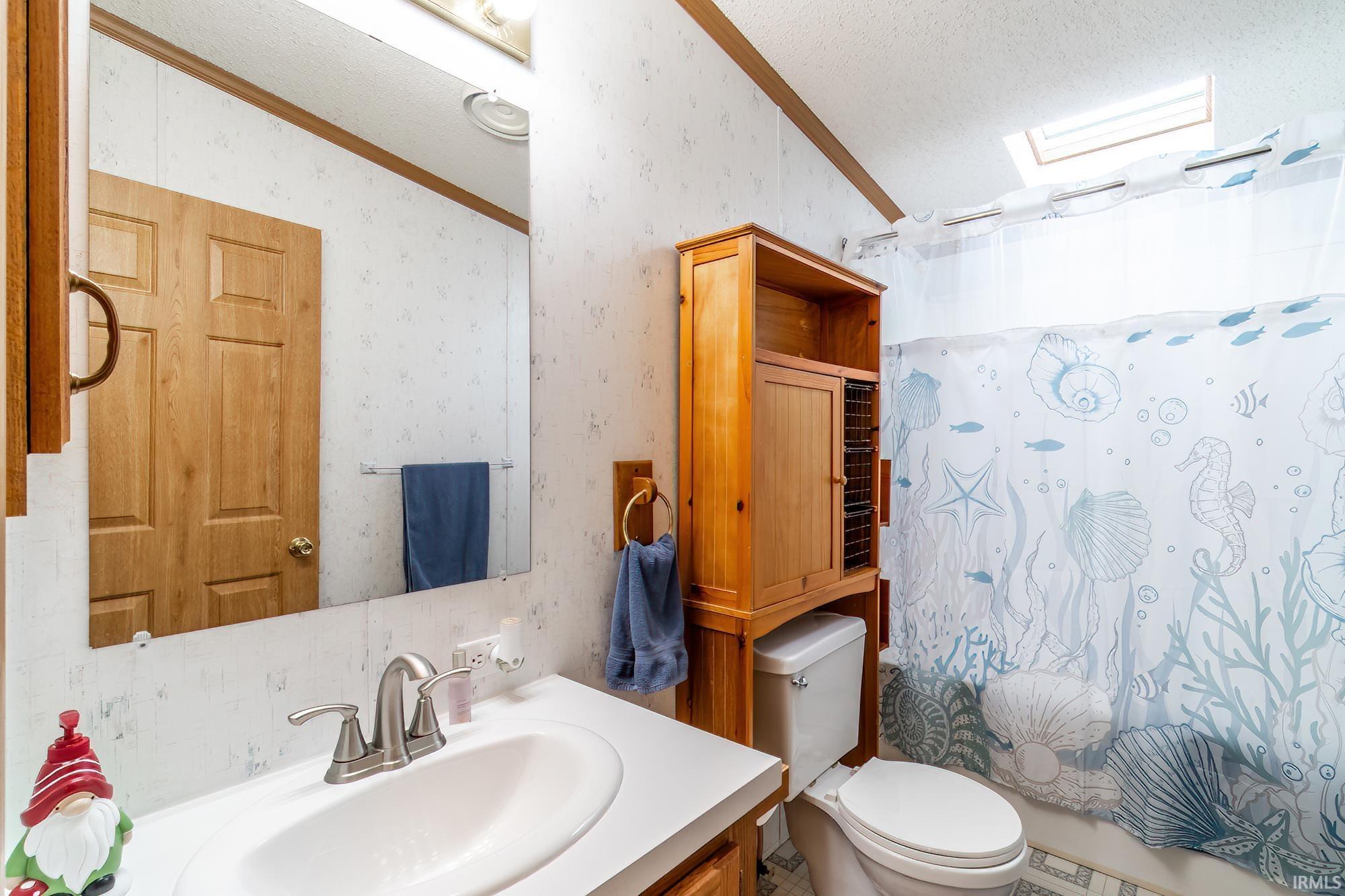 Bathroom with vanity, wallpapered walls, a textured ceiling, shower / bath combination with curtain, and crown molding