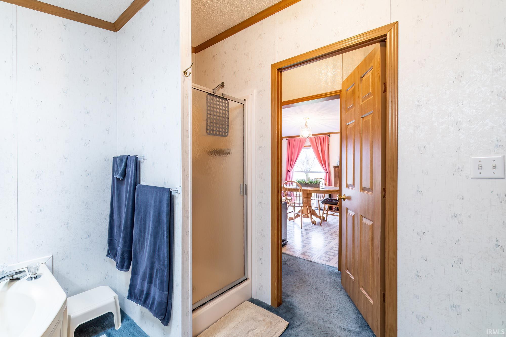 Bathroom with wallpapered walls, crown molding, a shower stall, and carpet