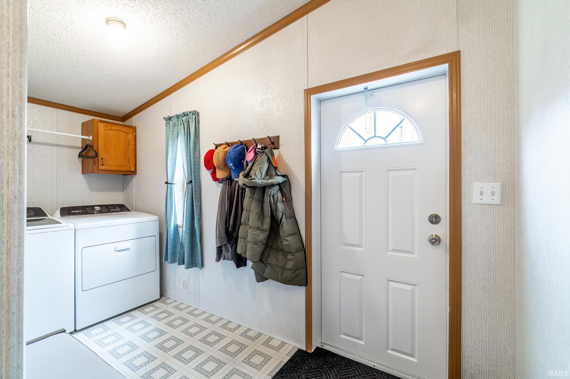 Washroom featuring a textured ceiling, ornamental molding, washer and clothes dryer, lofted ceiling, and light flooring