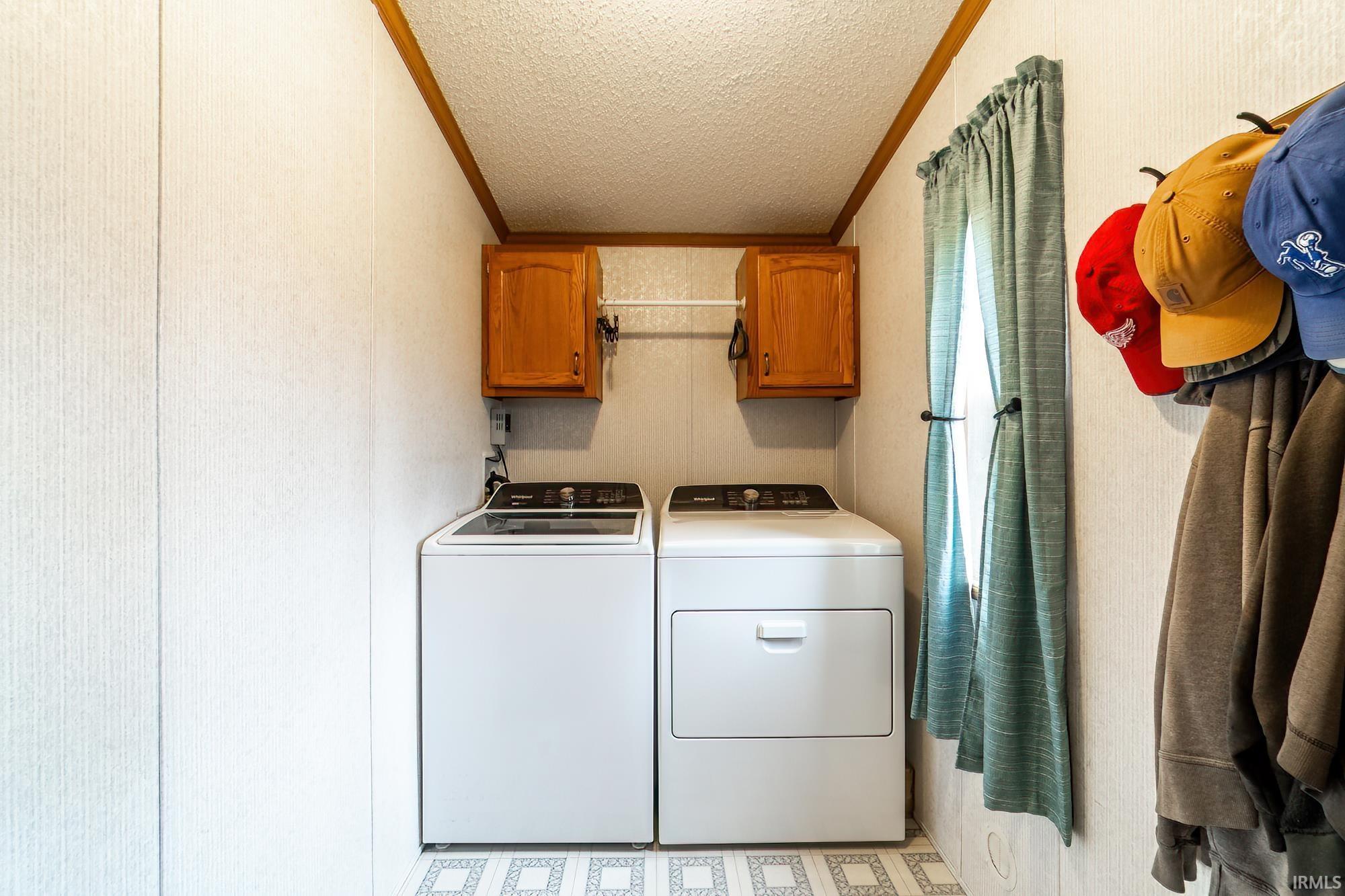 Laundry room featuring crown molding, cabinet space, a textured ceiling, and washing machine and clothes dryer