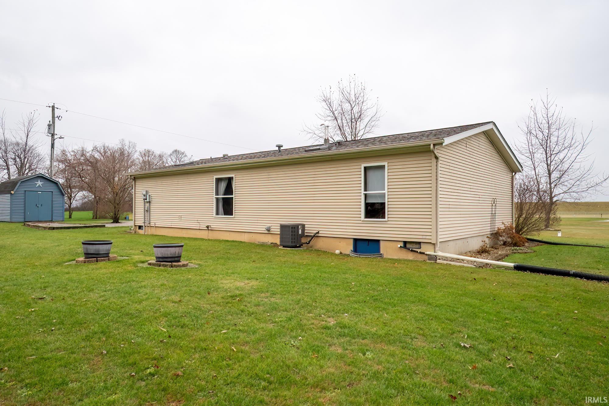 Rear view of property with a lawn, an outdoor fire pit, and a storage unit