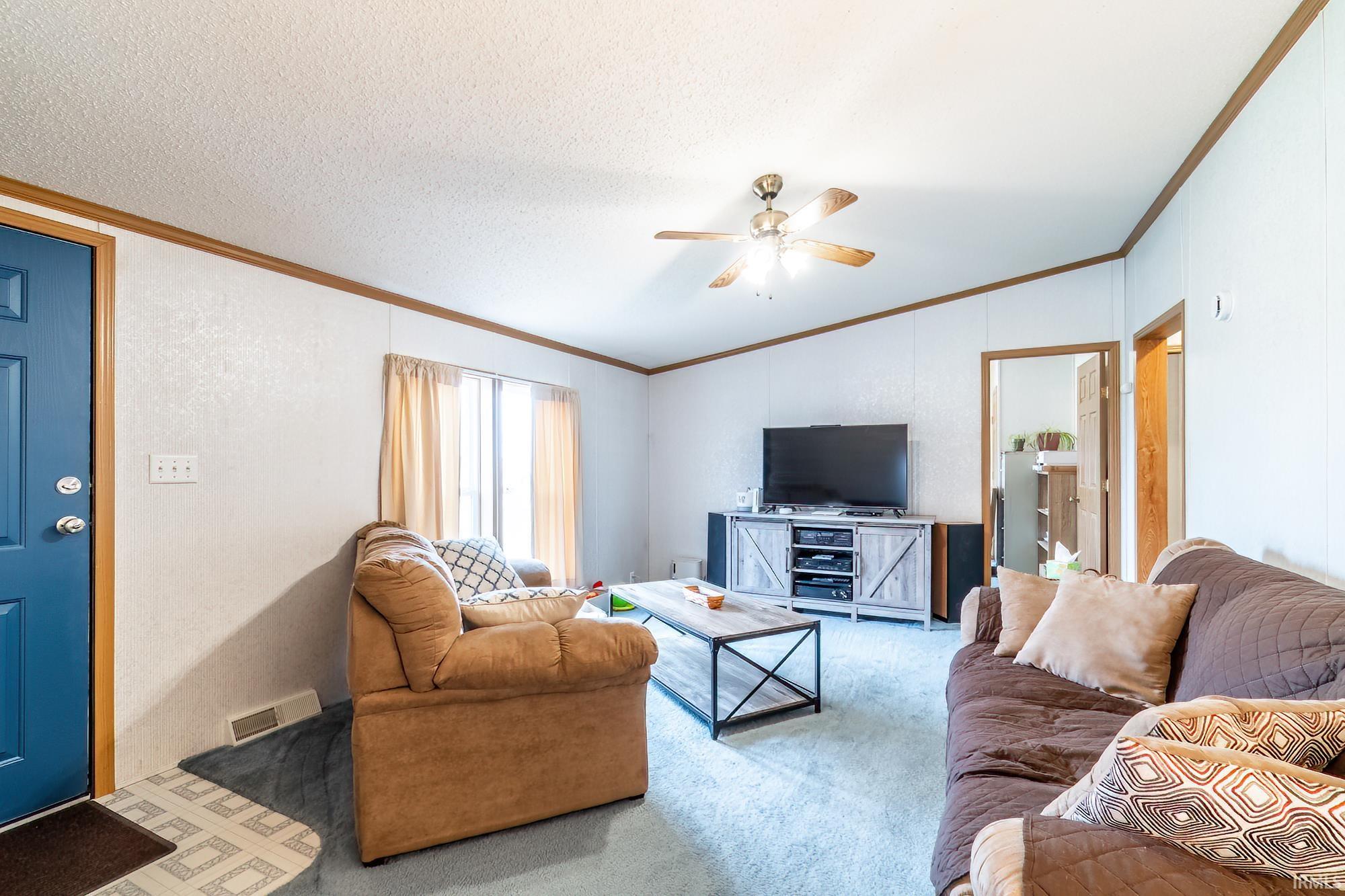 Carpeted living area with ornamental molding, lofted ceiling, a ceiling fan, a textured ceiling, and a textured wall