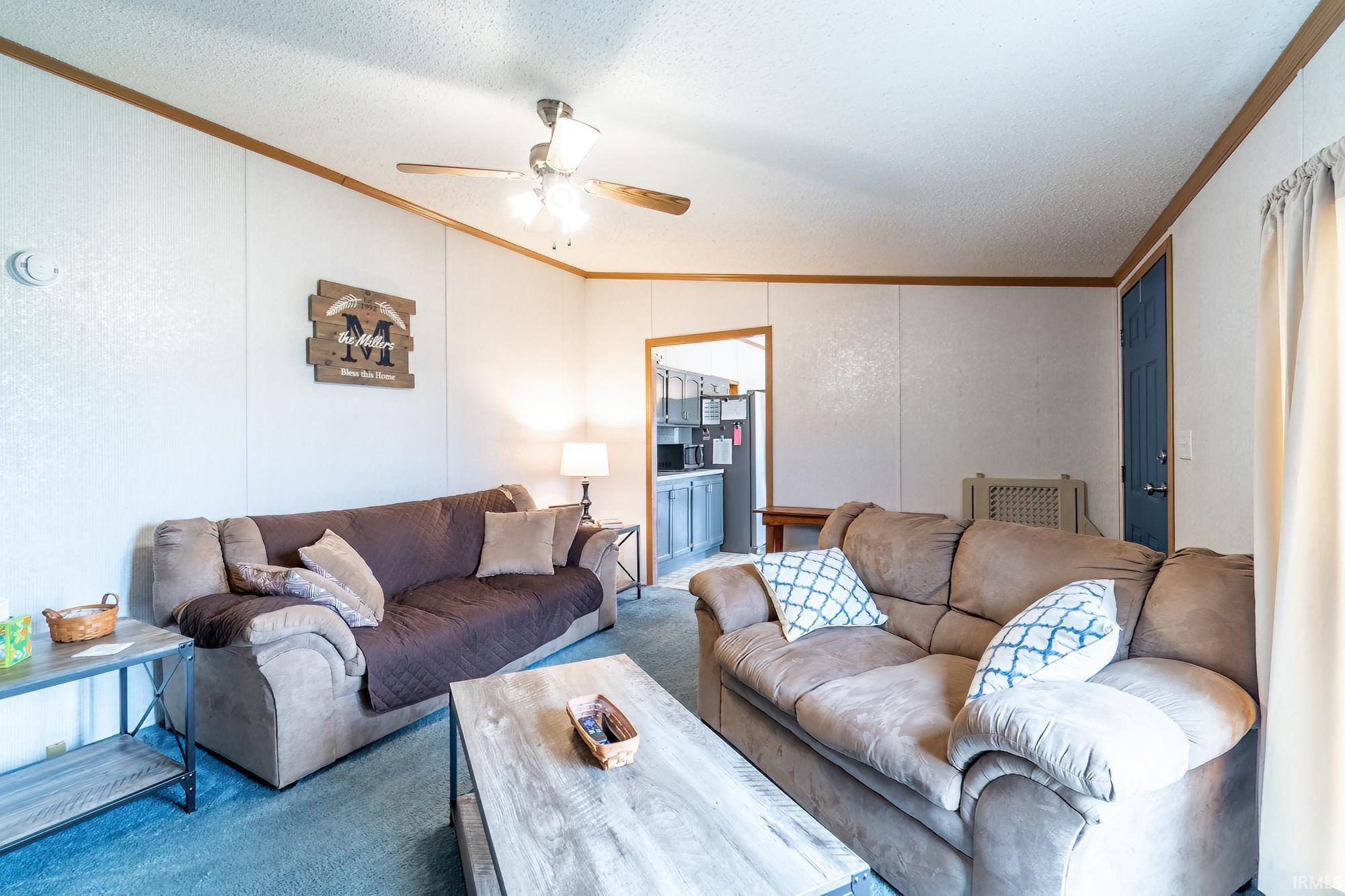 Living area with crown molding, vaulted ceiling, carpet flooring, a ceiling fan, and a textured ceiling
