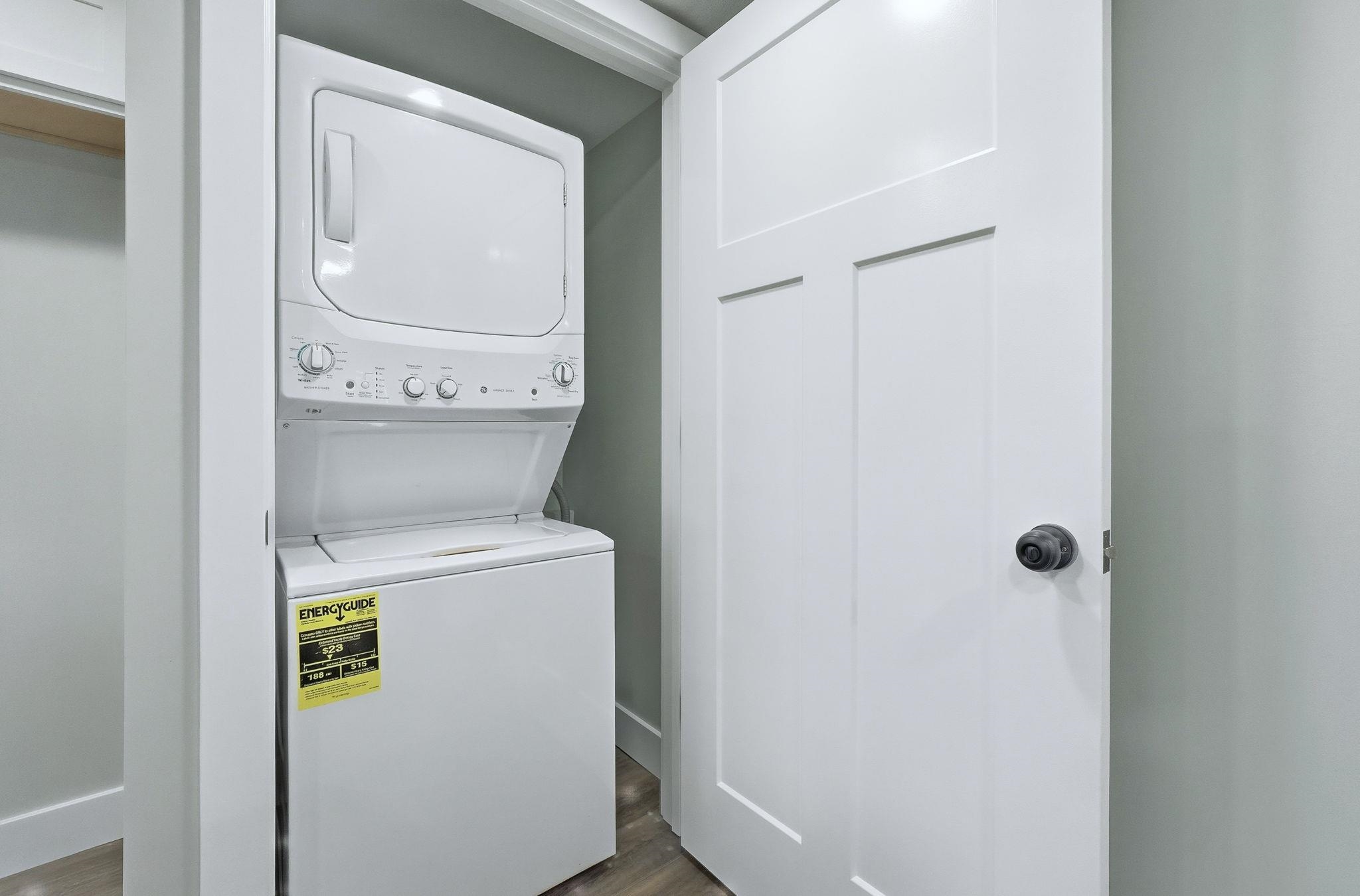 Laundry room with stacked washing machine and dryer and wood finished floors