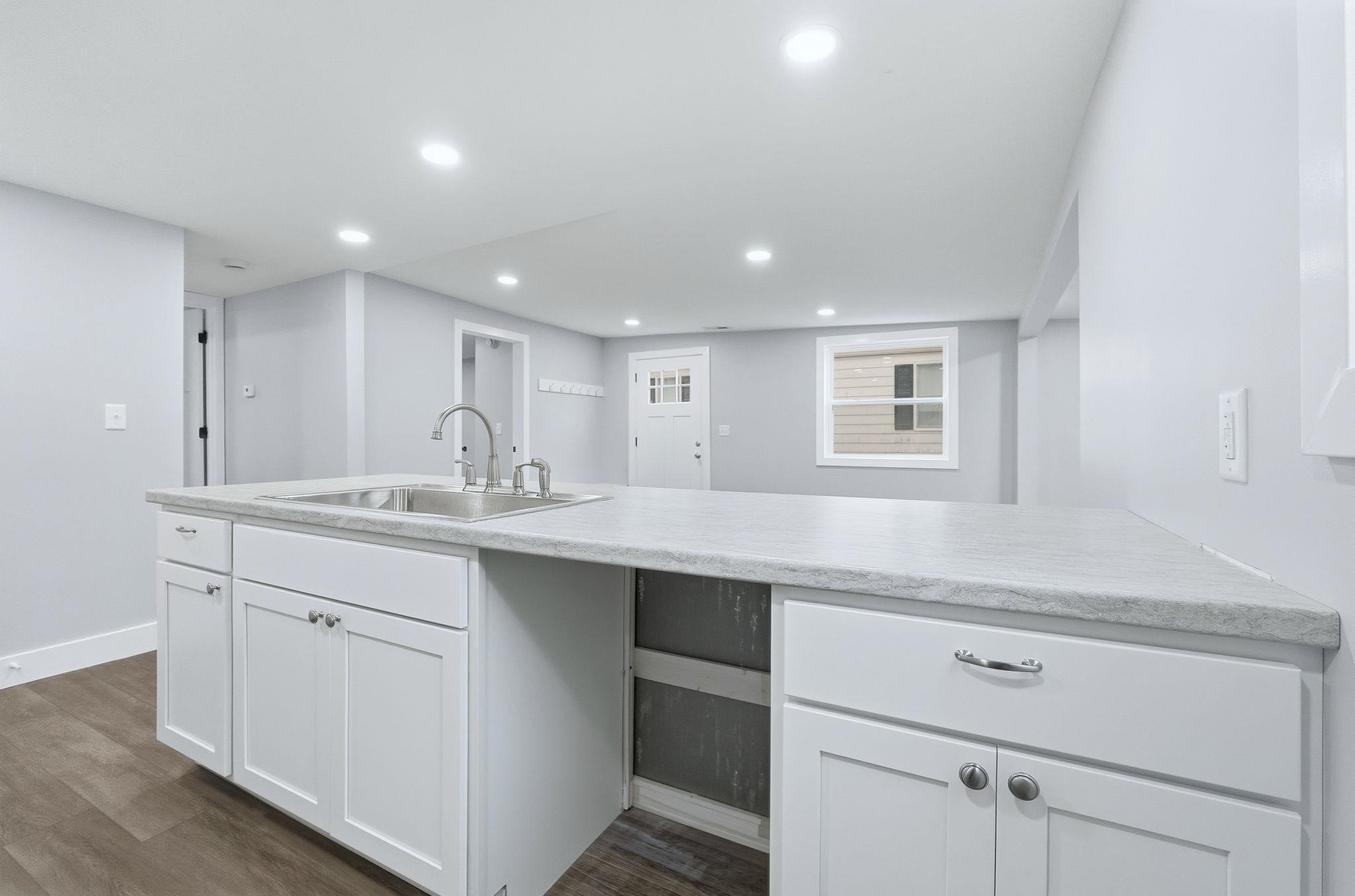 Kitchen with light countertops, a peninsula, white cabinets, dark wood-style flooring, and recessed lighting