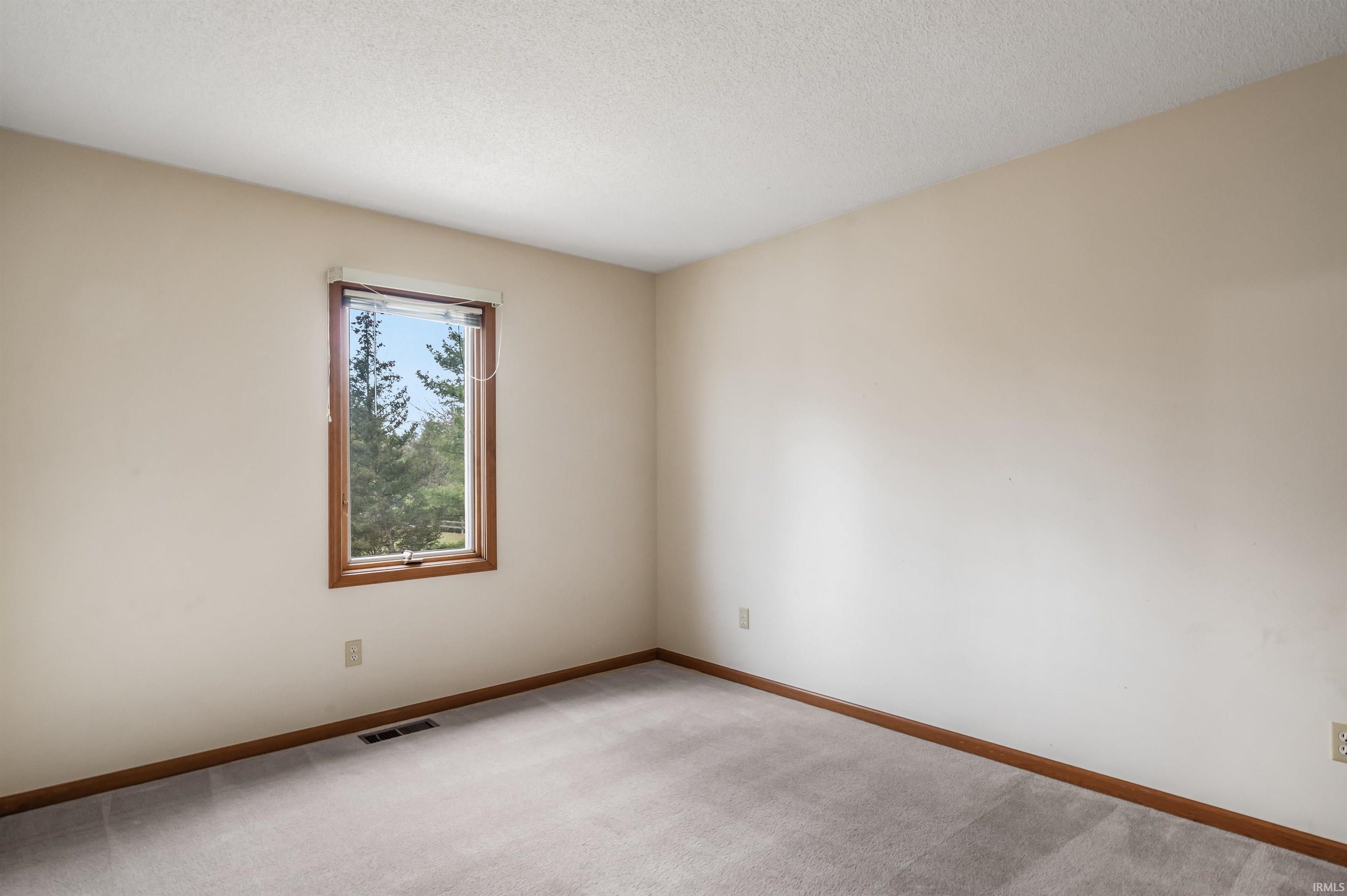 Carpeted empty room featuring a textured ceiling and baseboards