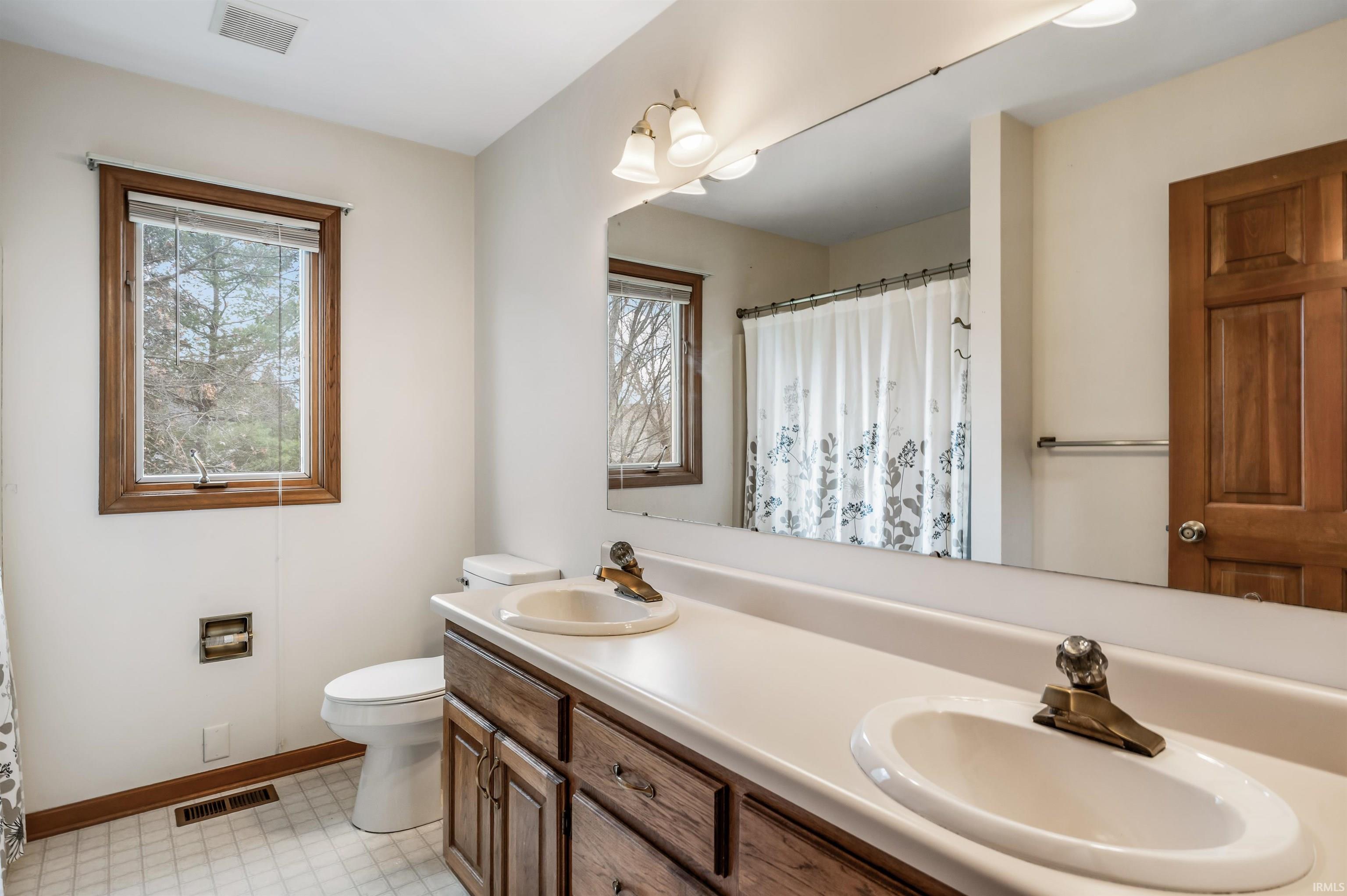 Full bathroom featuring a shower with curtain, double vanity, light flooring, and plenty of natural light