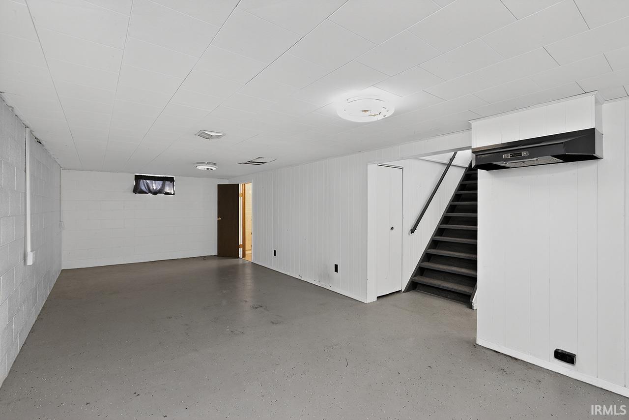 Finished basement with concrete block wall, stairway, and wood walls