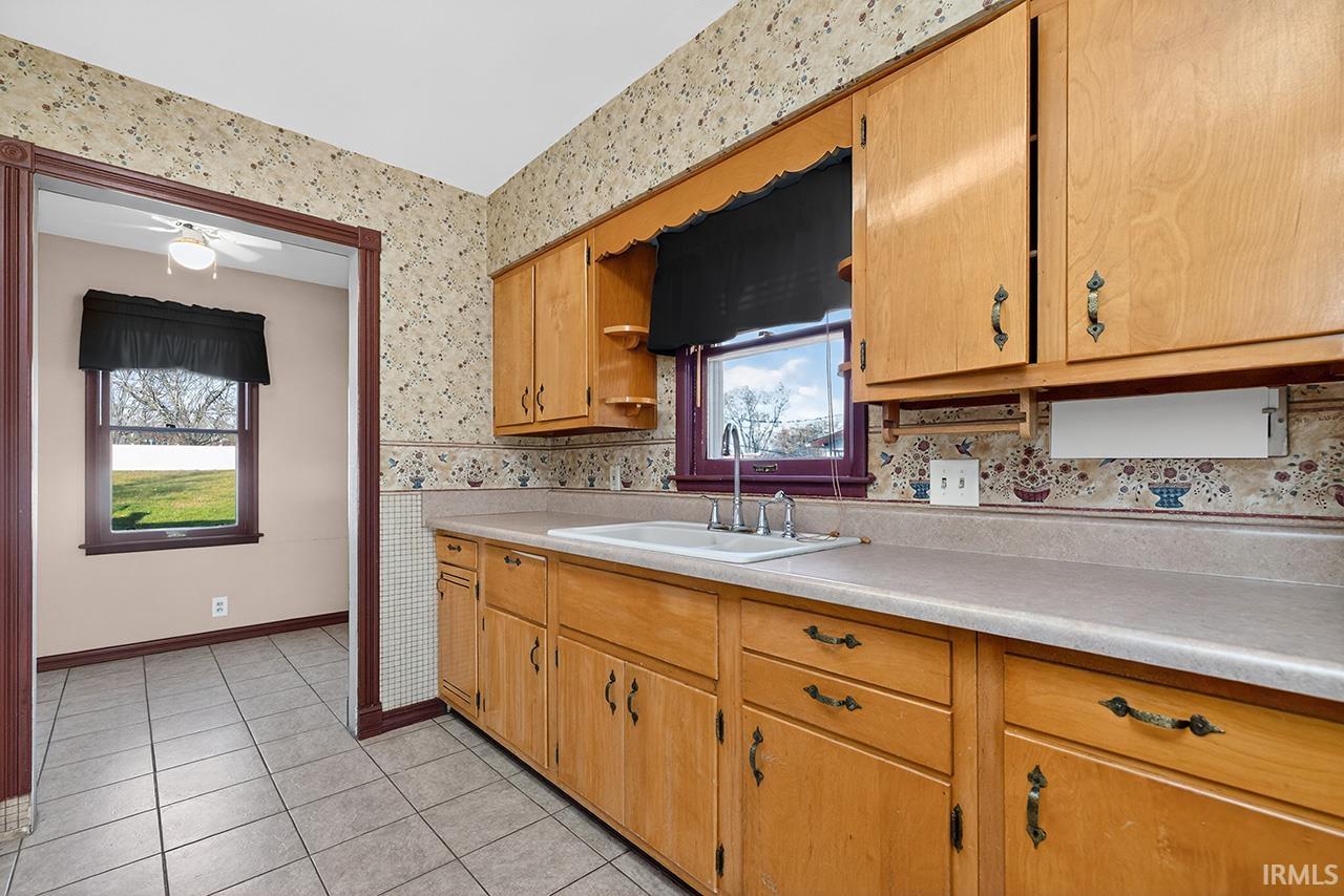 Kitchen with wallpapered walls, light countertops, light tile patterned floors, and brown cabinets