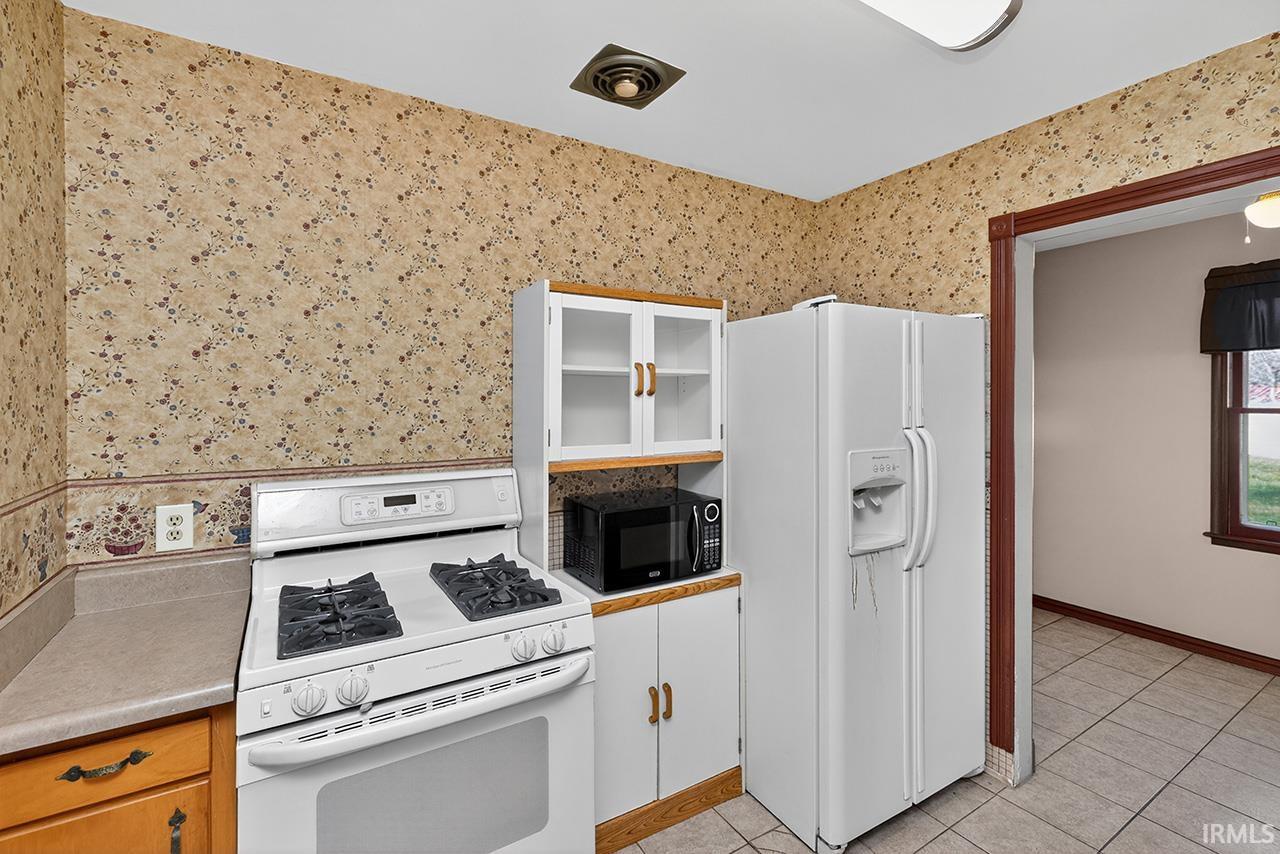 Kitchen with wallpapered walls, white appliances, white cabinets, and light countertops