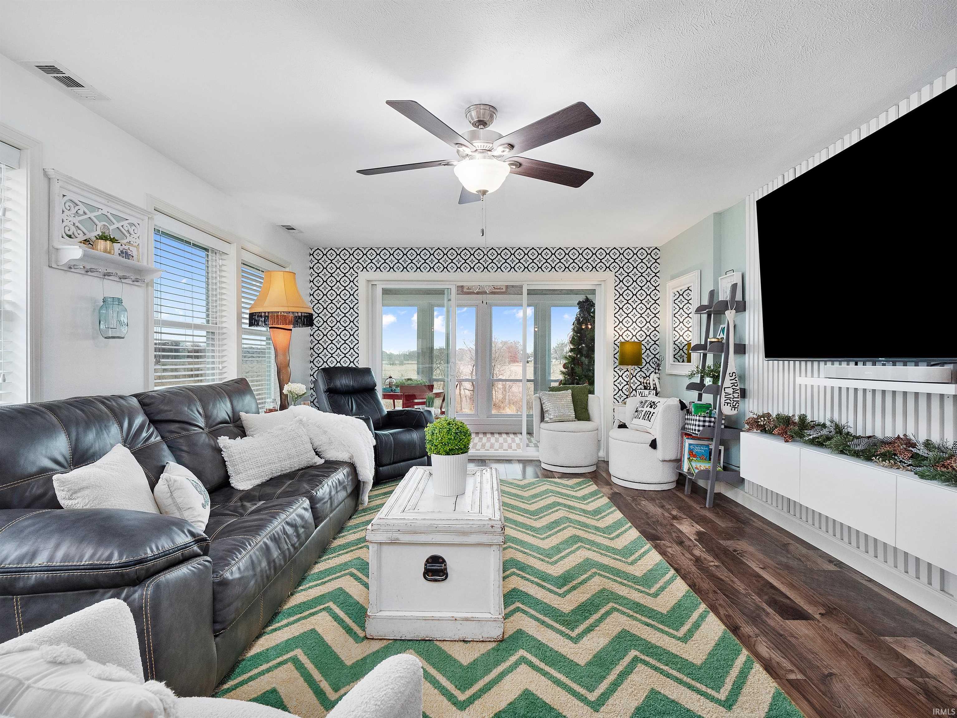 Living area featuring wallpapered walls, healthy amount of natural light, dark wood-style flooring, and ceiling fan