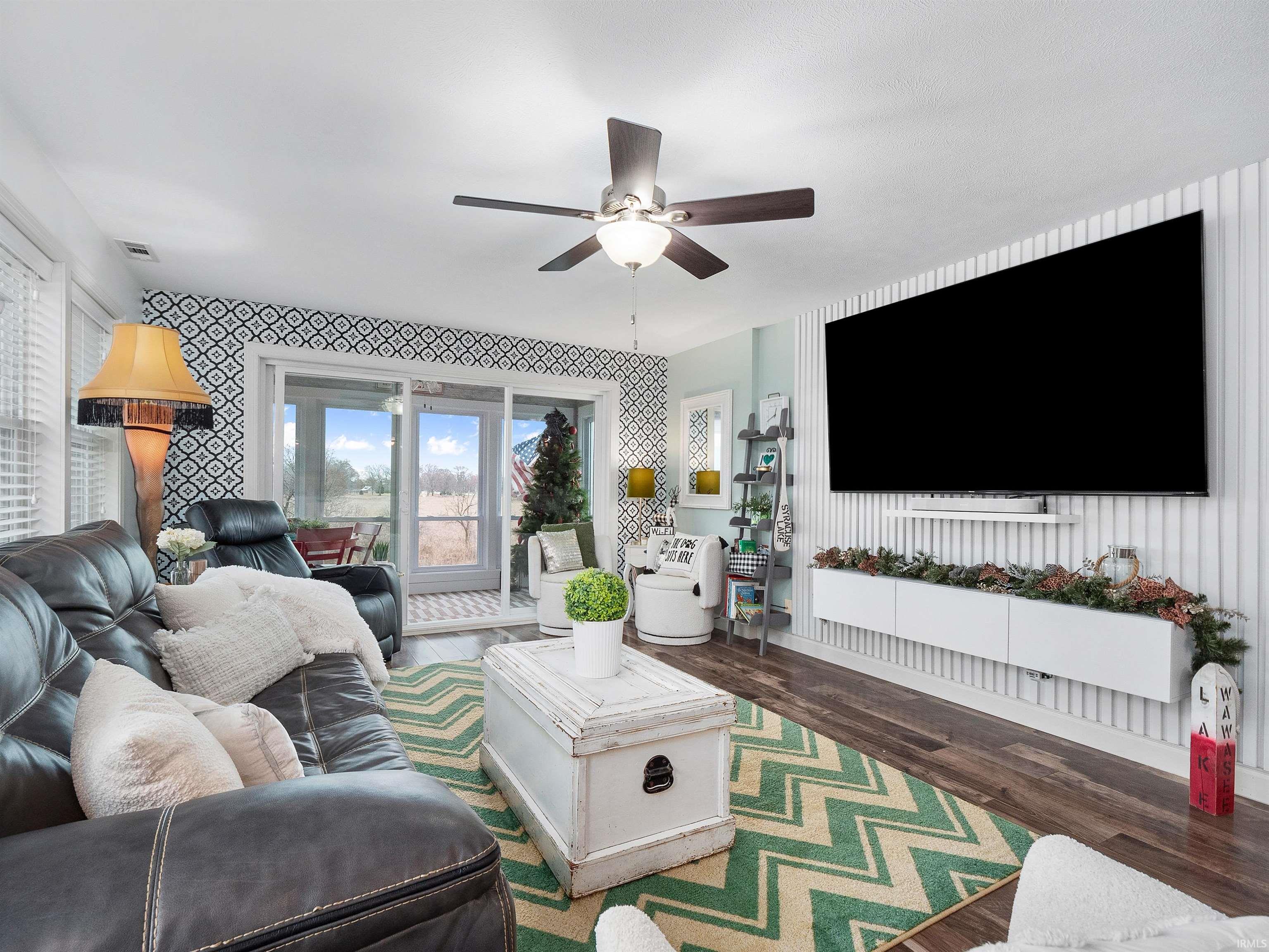 Living area featuring ceiling fan, dark wood-type flooring, wallpapered walls, and an accent wall