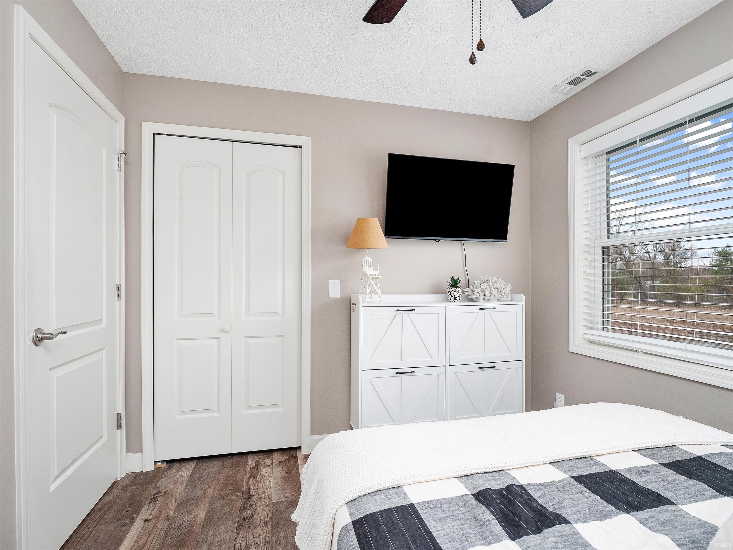 Bedroom with dark wood finished floors, ceiling fan, a textured ceiling, and a closet
