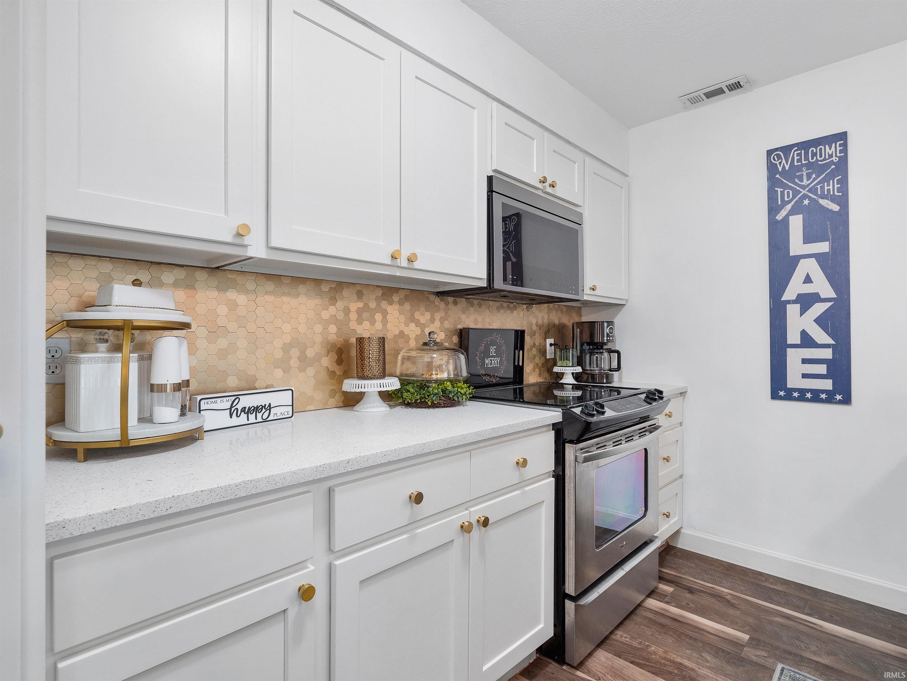 Kitchen with stainless steel appliances, decorative backsplash, white cabinets, dark wood finished floors, and light stone counters