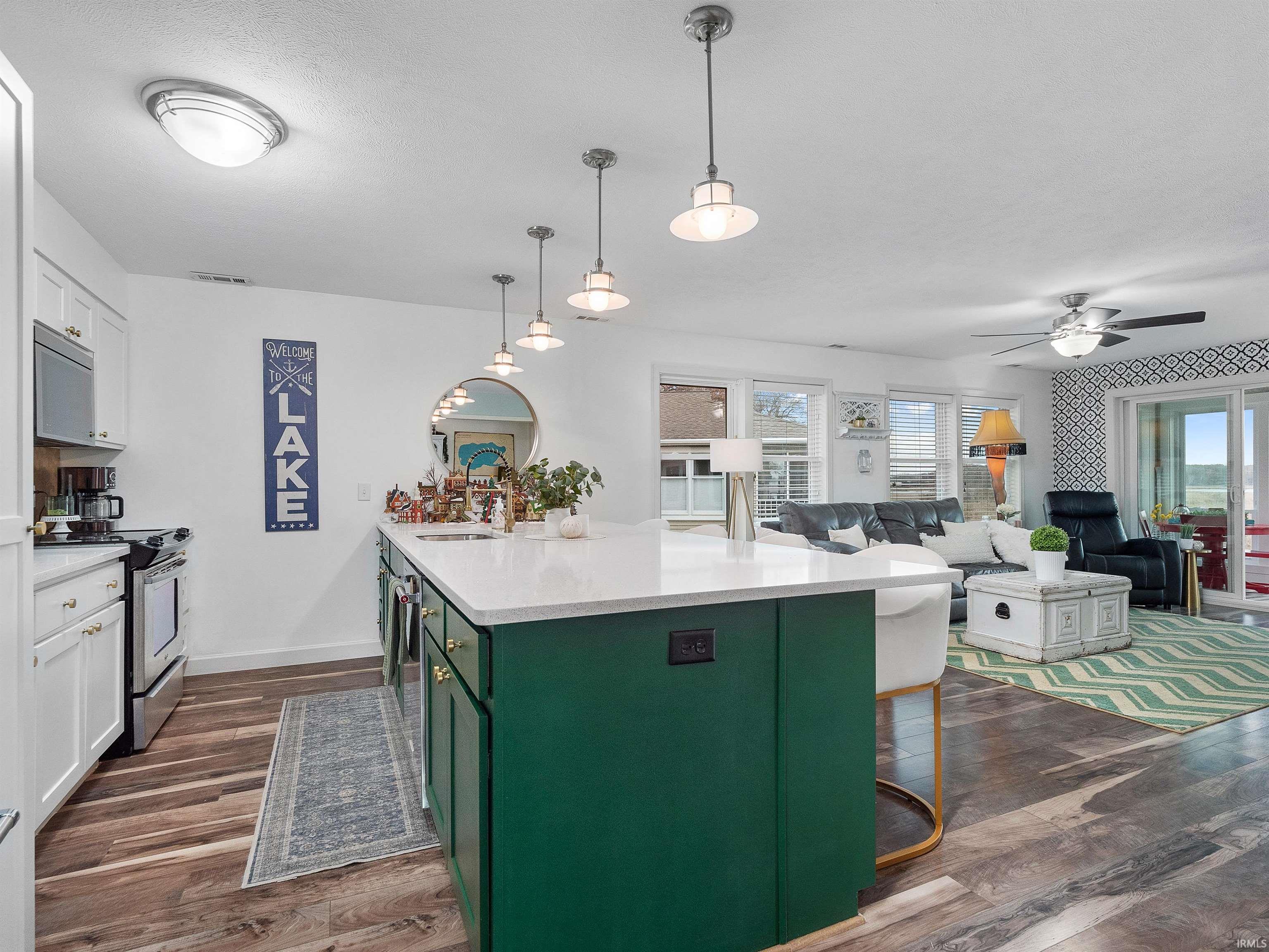 Kitchen featuring green cabinets, pendant lighting, stainless steel electric stove, white cabinetry, and a kitchen breakfast bar